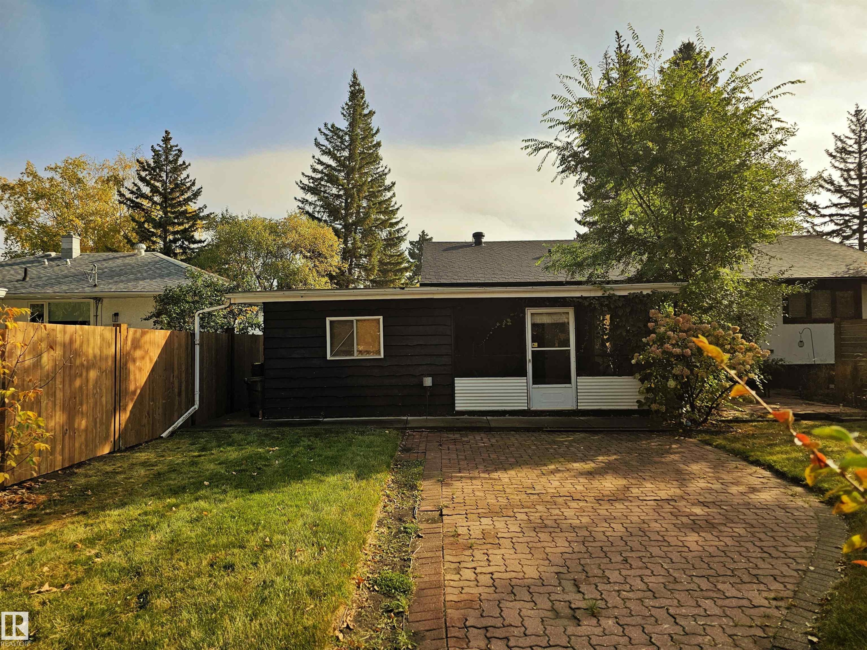 The property features a dark exterior with white trim, a paved brick driveway, a well-maintained lawn, and mature trees - 8604 142 Street, Edmonton, AB - Outdoor
