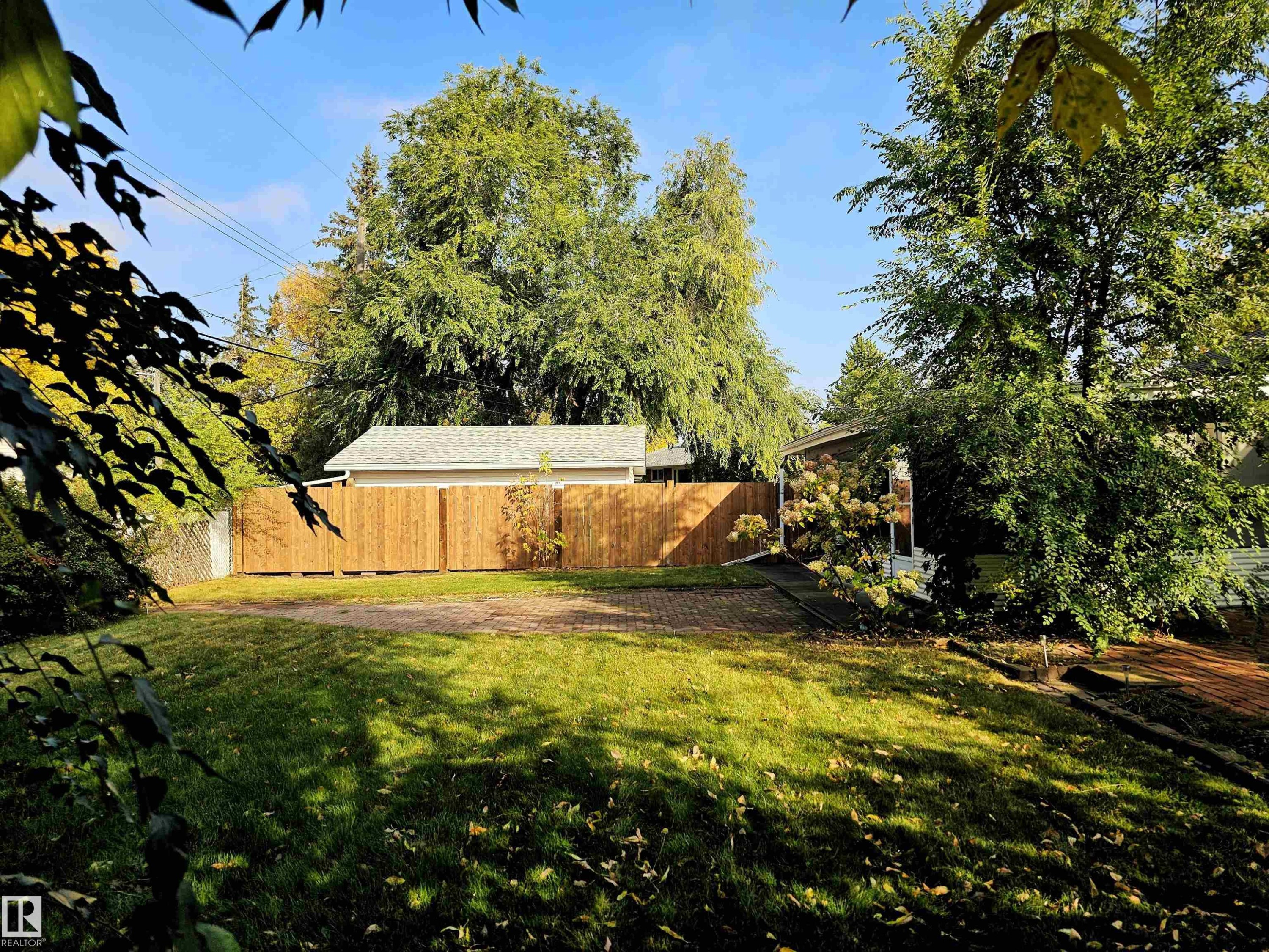 The property features a well-maintained lawn, a new wood fence, and mature trees - 8604 142 Street, Edmonton, AB - Outdoor