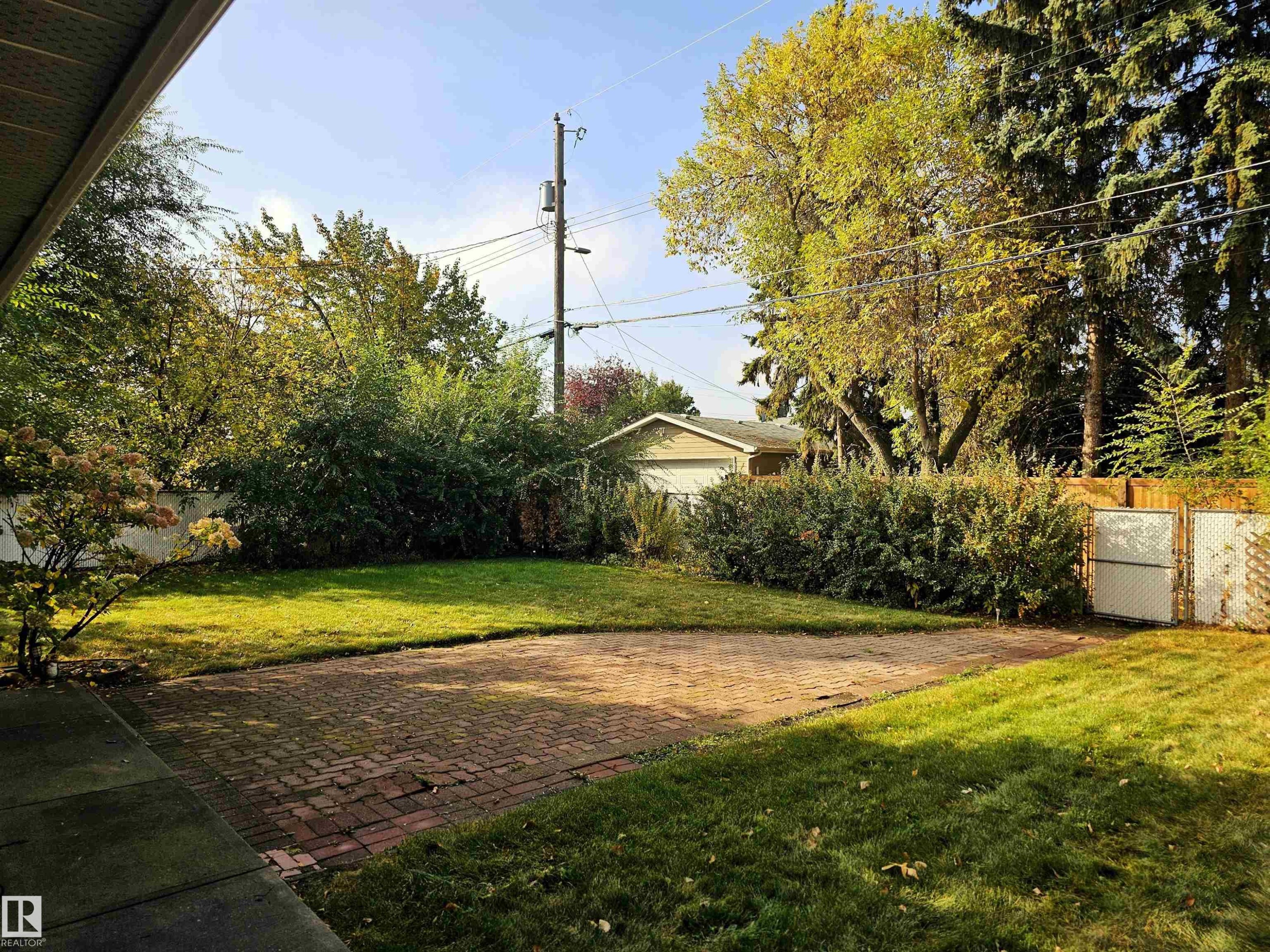 The property features a spacious yard with a lawn, mature trees, and a brick patio - 8604 142 Street, Edmonton, AB - Outdoor