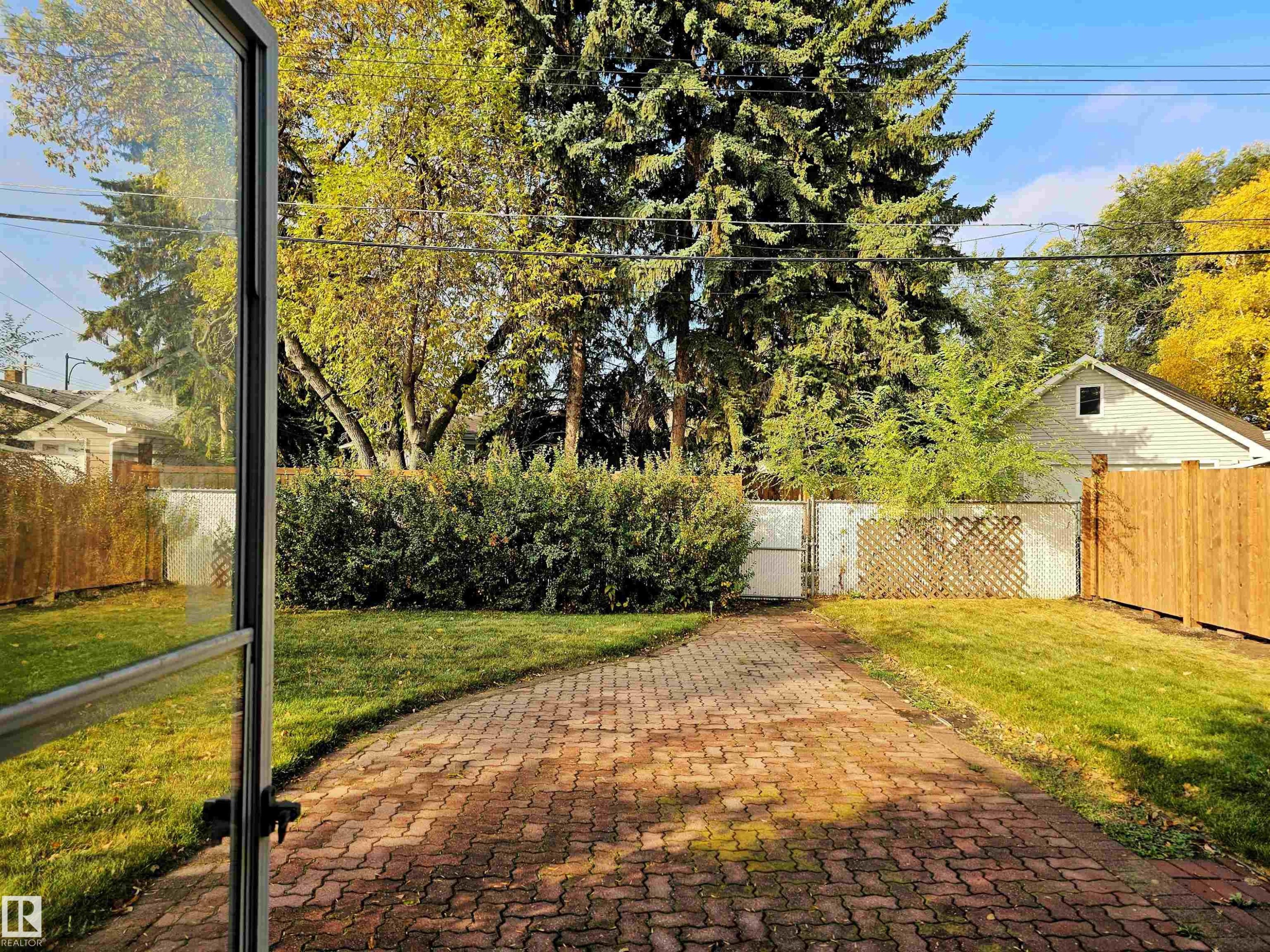 The property features a brick paver pathway and a well-maintained lawn, surrounded by lush green foliage and mature trees - 8604 142 Street, Edmonton, AB - Outdoor