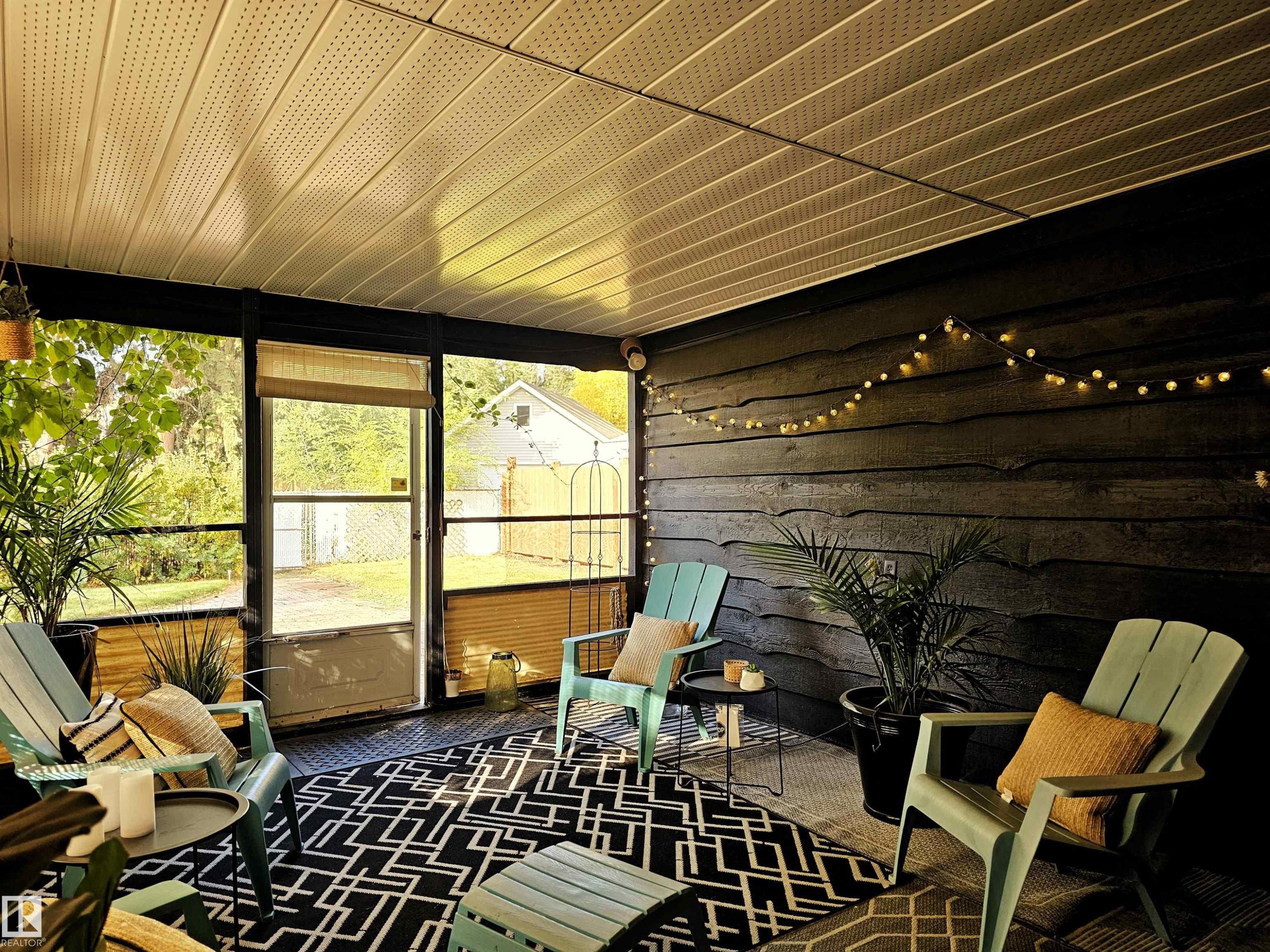 The screened-in porch offers a comfortable outdoor living space with a black and white patterned rug, a dark wood wall with string lights, and a light-colored ceiling - 8604 142 Street, Edmonton, AB - With Exterior