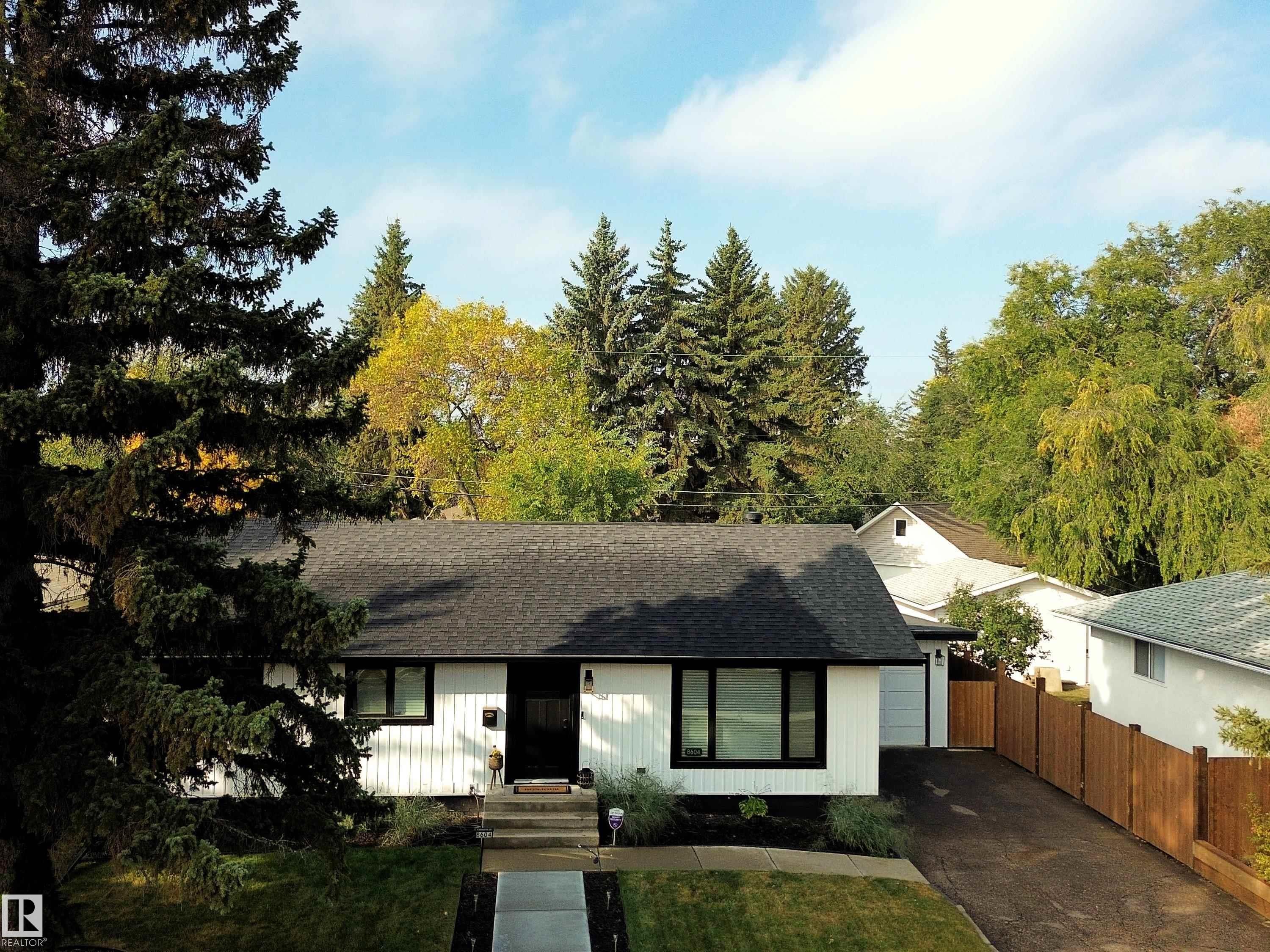 The property features a white exterior with black trim, a dark shingle roof, and a front yard with a lawn and landscaping - 8604 142 Street, Edmonton, AB - Outdoor