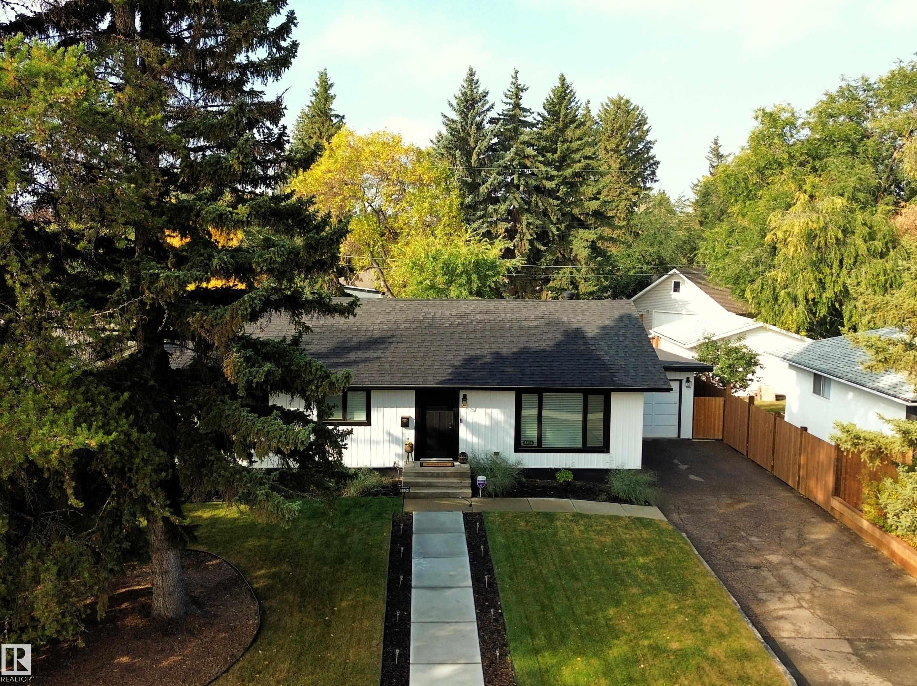 The property features a white exterior with a black roof, dark-framed windows, and a black front door, complemented by a concrete walkway leading to the entrance - 8604 142 Street, Edmonton, AB - Outdoor