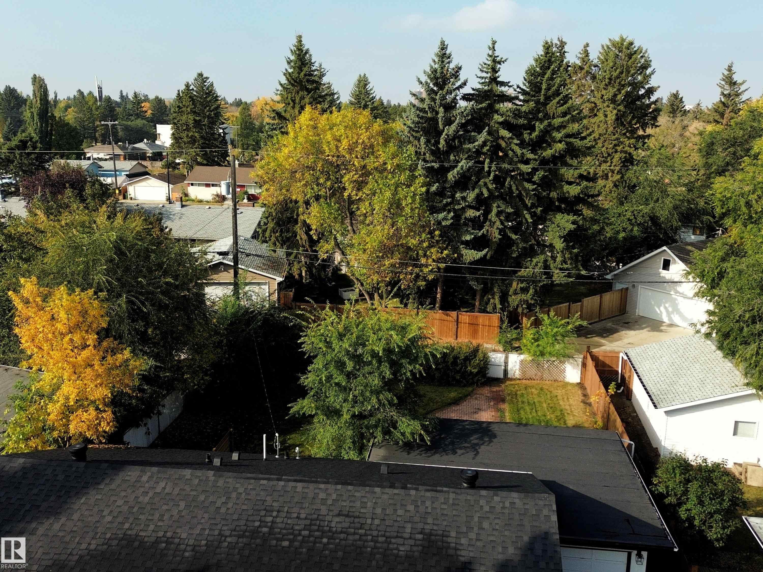 The property features a dark shingle roof and is surrounded by mature trees, with a view of other residential roofs and green spaces - 8604 142 Street, Edmonton, AB - Outdoor