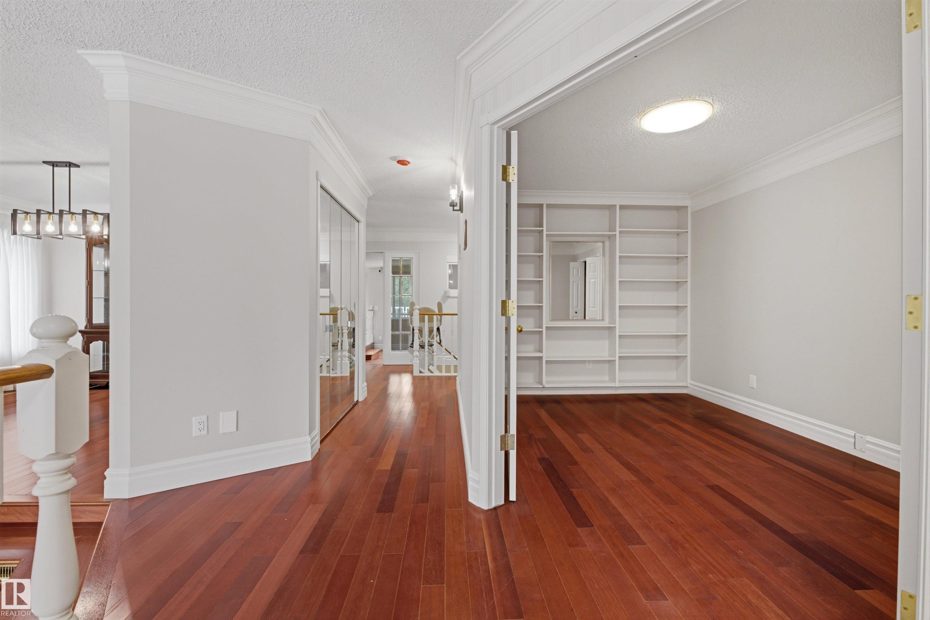 Hardwood flooring extends throughout this well-lit space, featuring crown molding, baseboards, and a room with built-in shelving - 131 Walsh Crescent, Edmonton, AB - Indoor Photo Showing Other Room