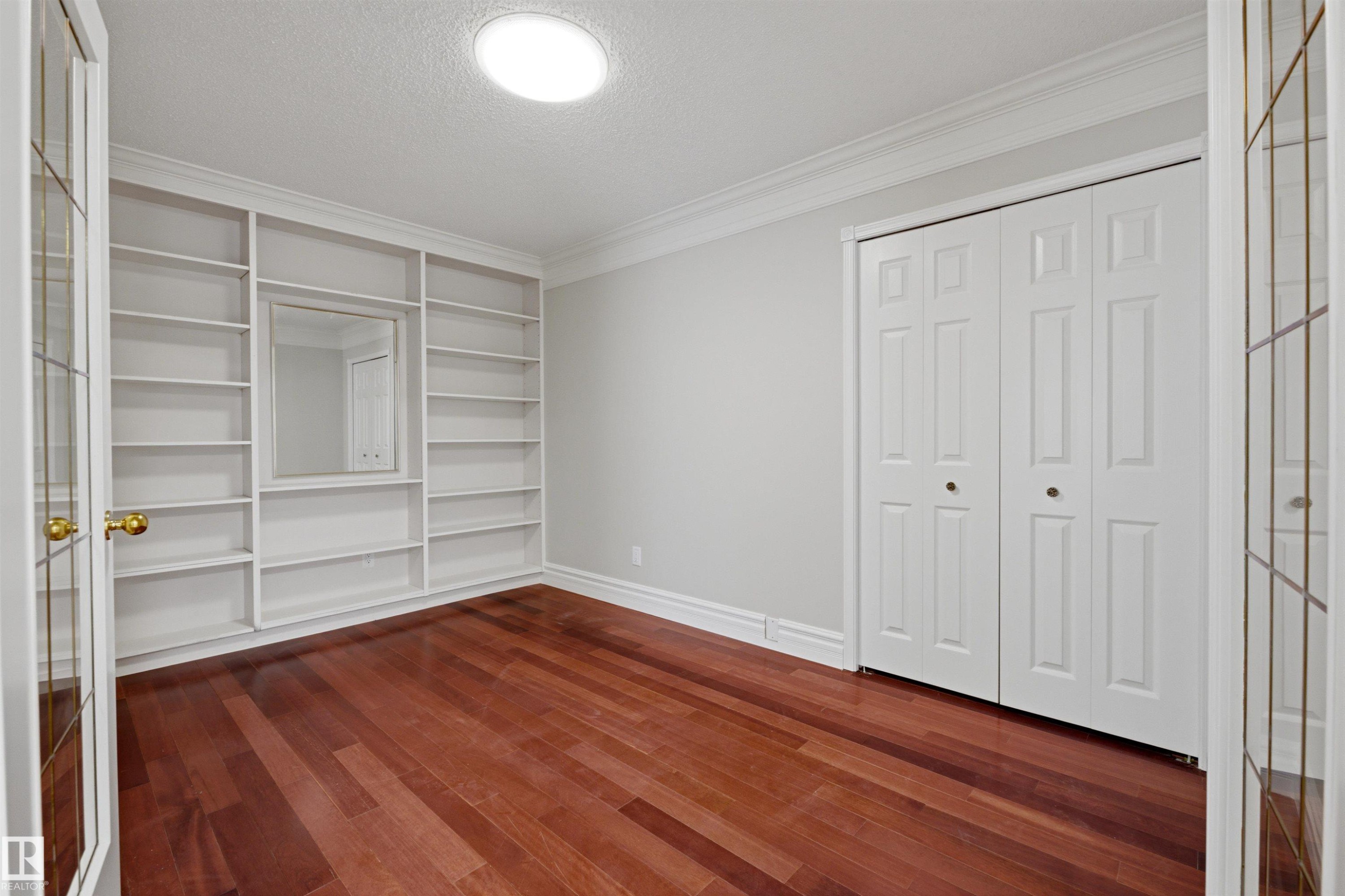 This room features rich hardwood flooring, built-in shelving, and white bi-fold closet doors - 131 Walsh Crescent, Edmonton, AB - Indoor Photo Showing Other Room