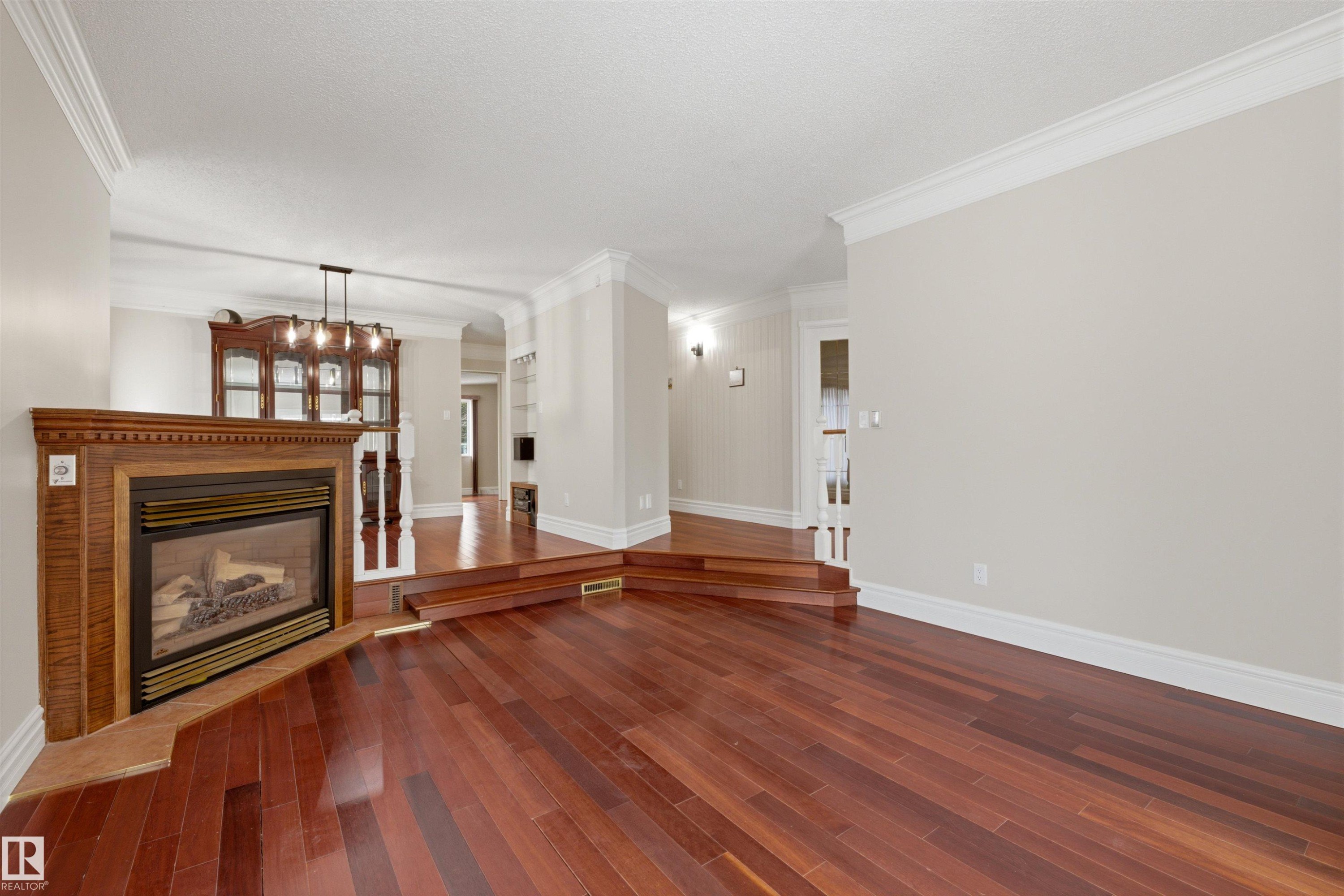 Living area featuring hardwood flooring, a fireplace with a wood surround, and crown molding - 131 Walsh Crescent, Edmonton, AB - Indoor Photo Showing Living Room With Fireplace