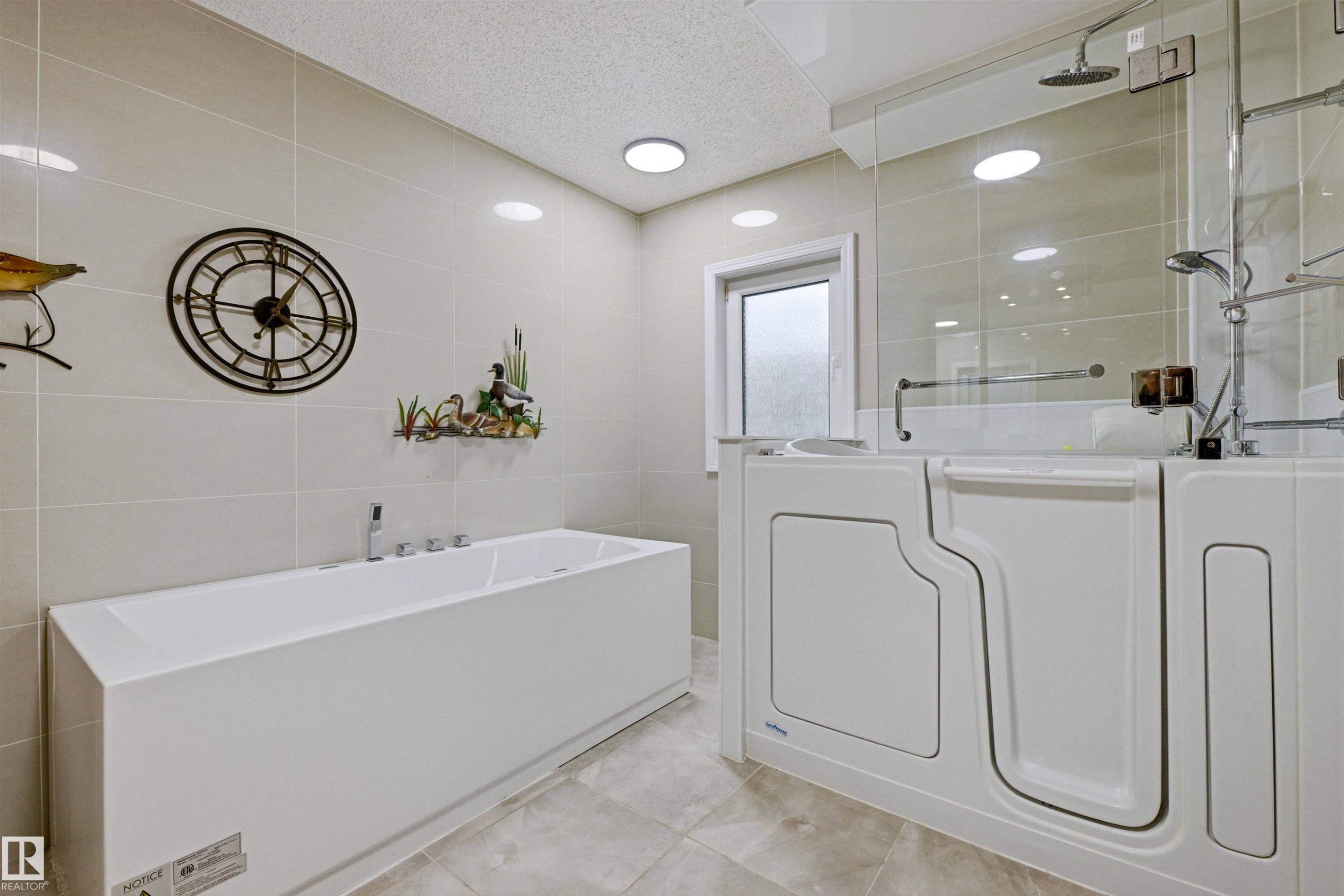 Bathroom featuring a white rectangular bathtub, a walk-in shower with clear glass enclosure, and light-colored tiled walls and floors - 131 Walsh Crescent, Edmonton, AB - Indoor Photo Showing Laundry Room