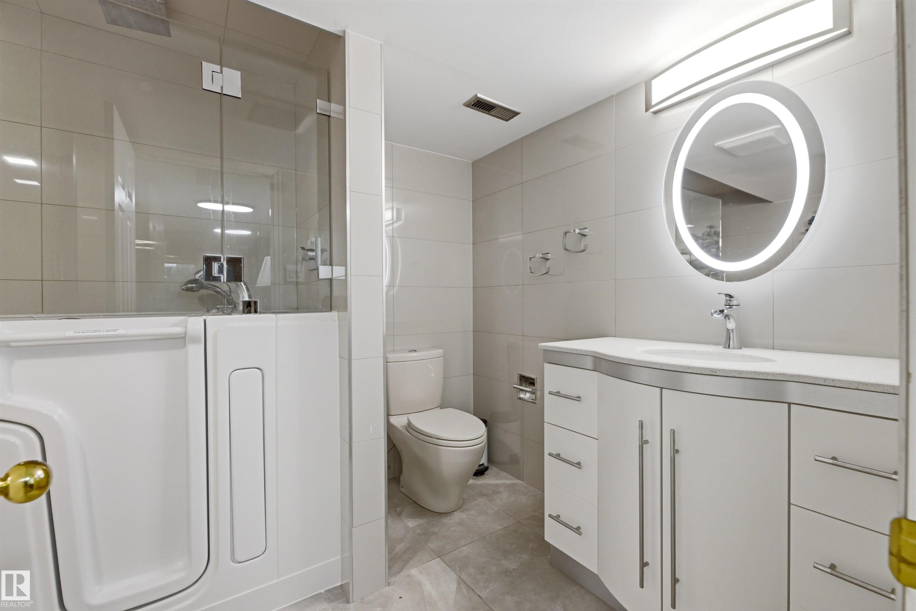 Bathroom featuring a walk-in tub with a glass enclosure, a contemporary vanity with a granite countertop, and an illuminated oval mirror - 131 Walsh Crescent, Edmonton, AB - Indoor Photo Showing Bathroom