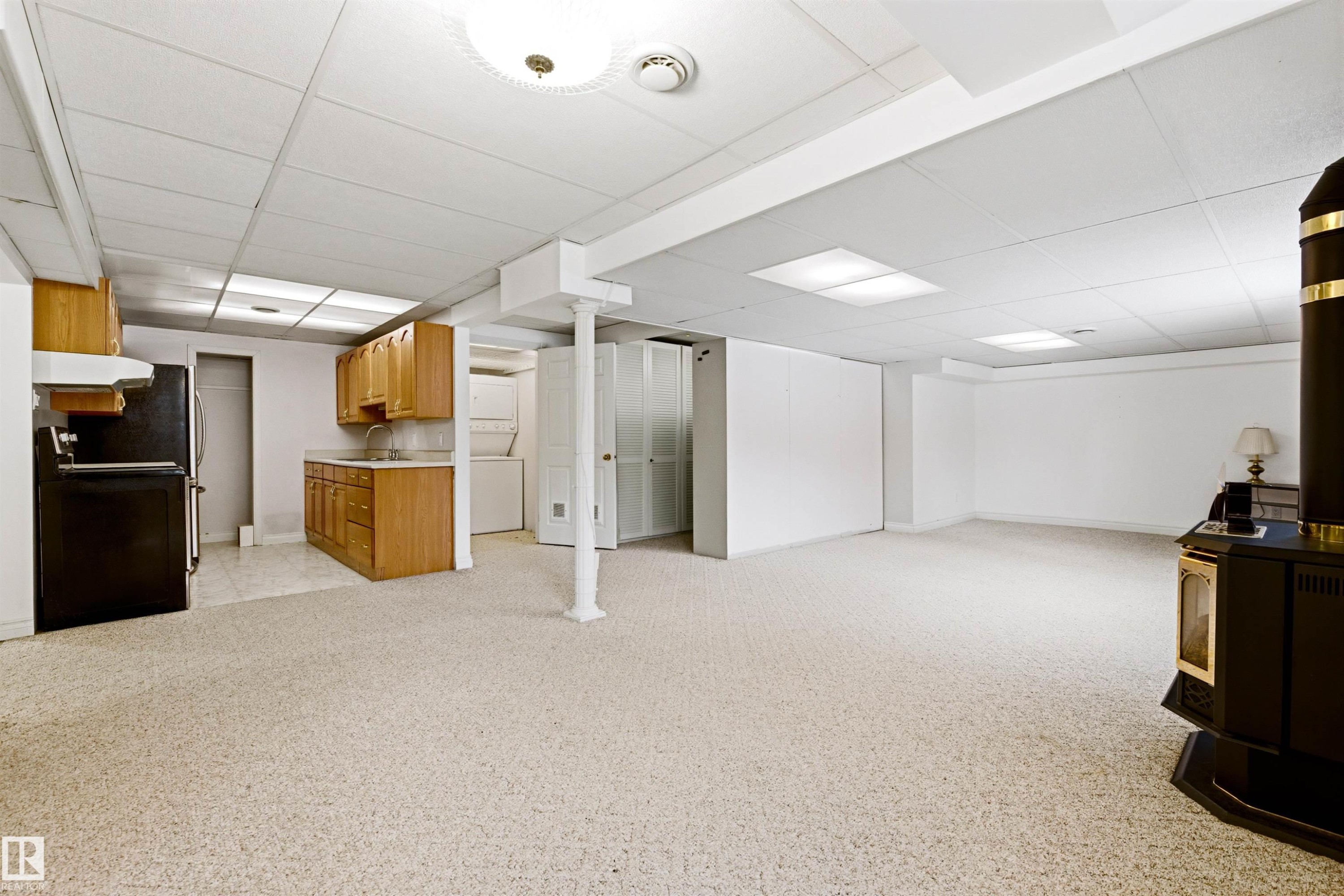 Expansive lower level featuring light-colored carpeting, recessed lighting, and a kitchen area with wooden cabinetry and a black refrigerator - 131 Walsh Crescent, Edmonton, AB - Indoor