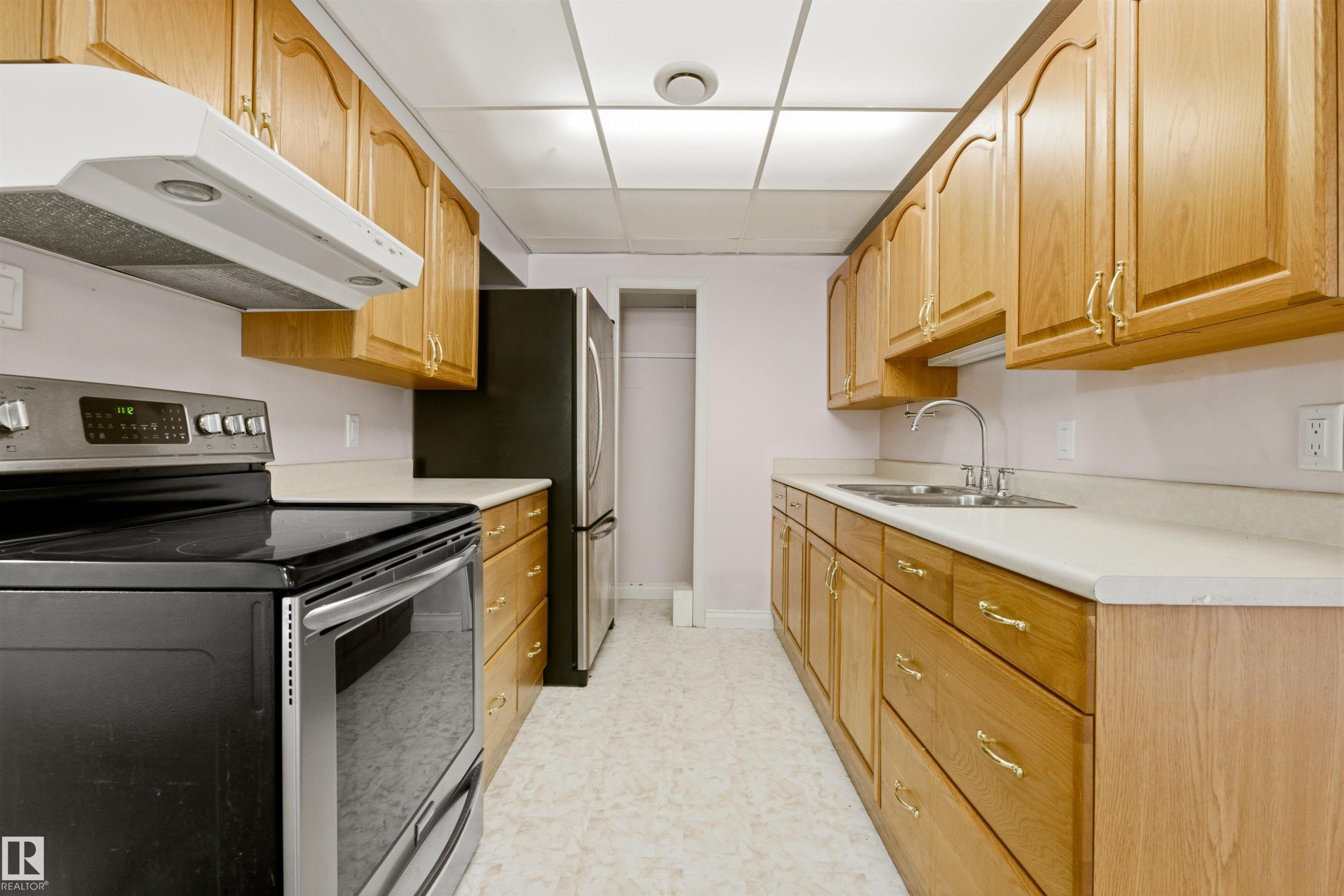 The kitchen features extensive natural wood cabinetry, light-colored countertops, a double basin stainless steel sink with a chrome faucet, and a black and stainless steel range - 131 Walsh Crescent, Edmonton, AB - Indoor Photo Showing Kitchen
