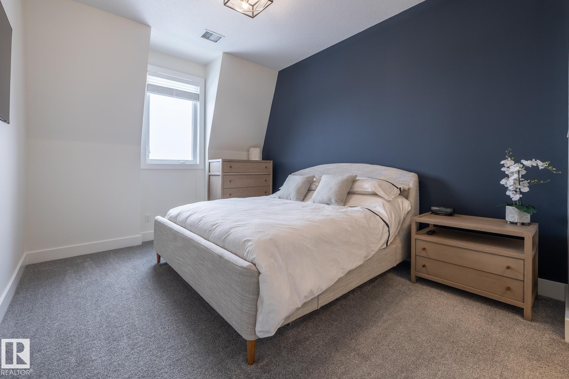 This bedroom features light gray carpeting, a window, and a dark accent wall - 454 6079 Maynard Way, Edmonton, AB - Indoor Photo Showing Bedroom