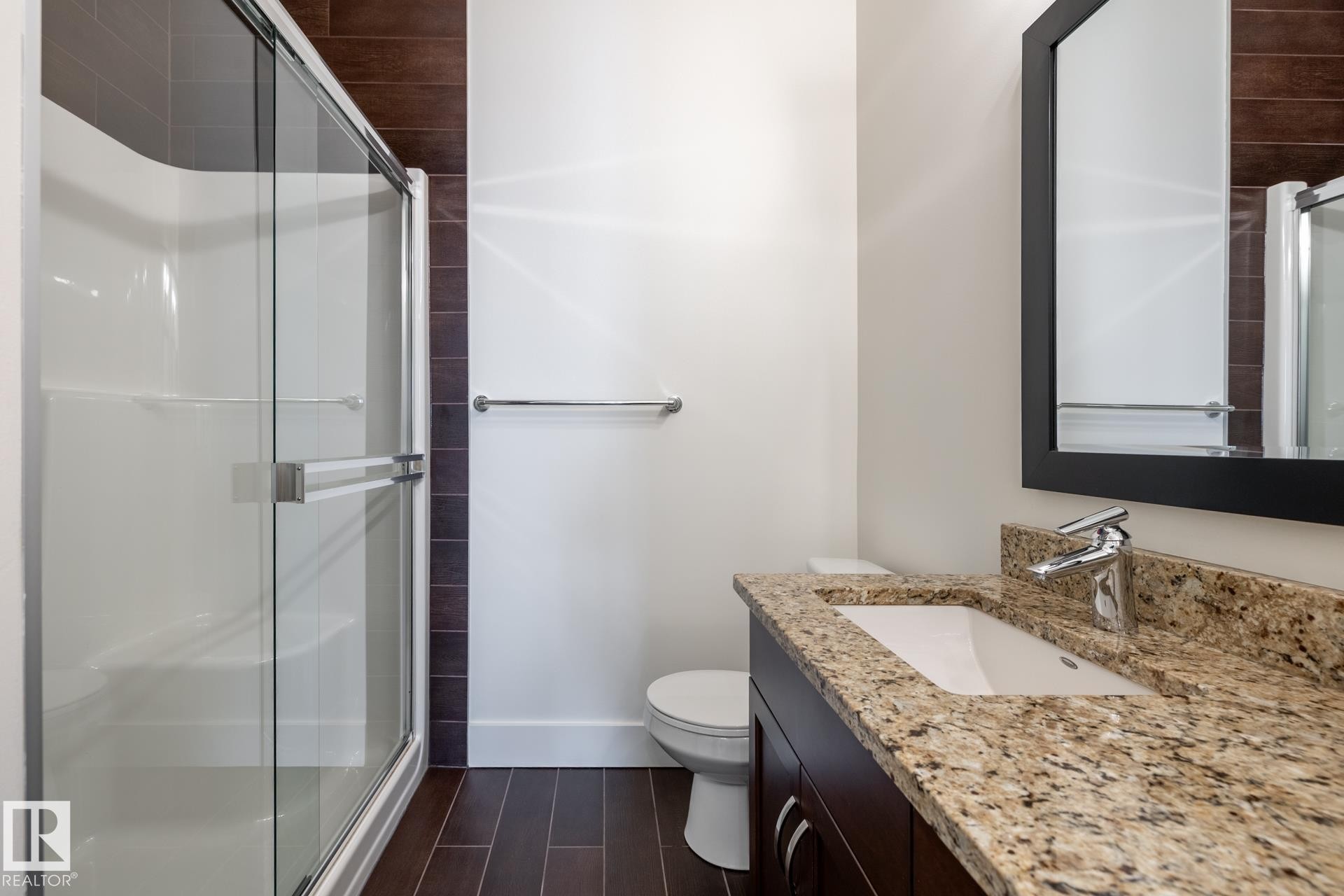 This bathroom features a shower with a sliding glass door, a vanity with a granite countertop, and a dark framed mirror - 454 6079 Maynard Way, Edmonton, AB - Indoor Photo Showing Bathroom