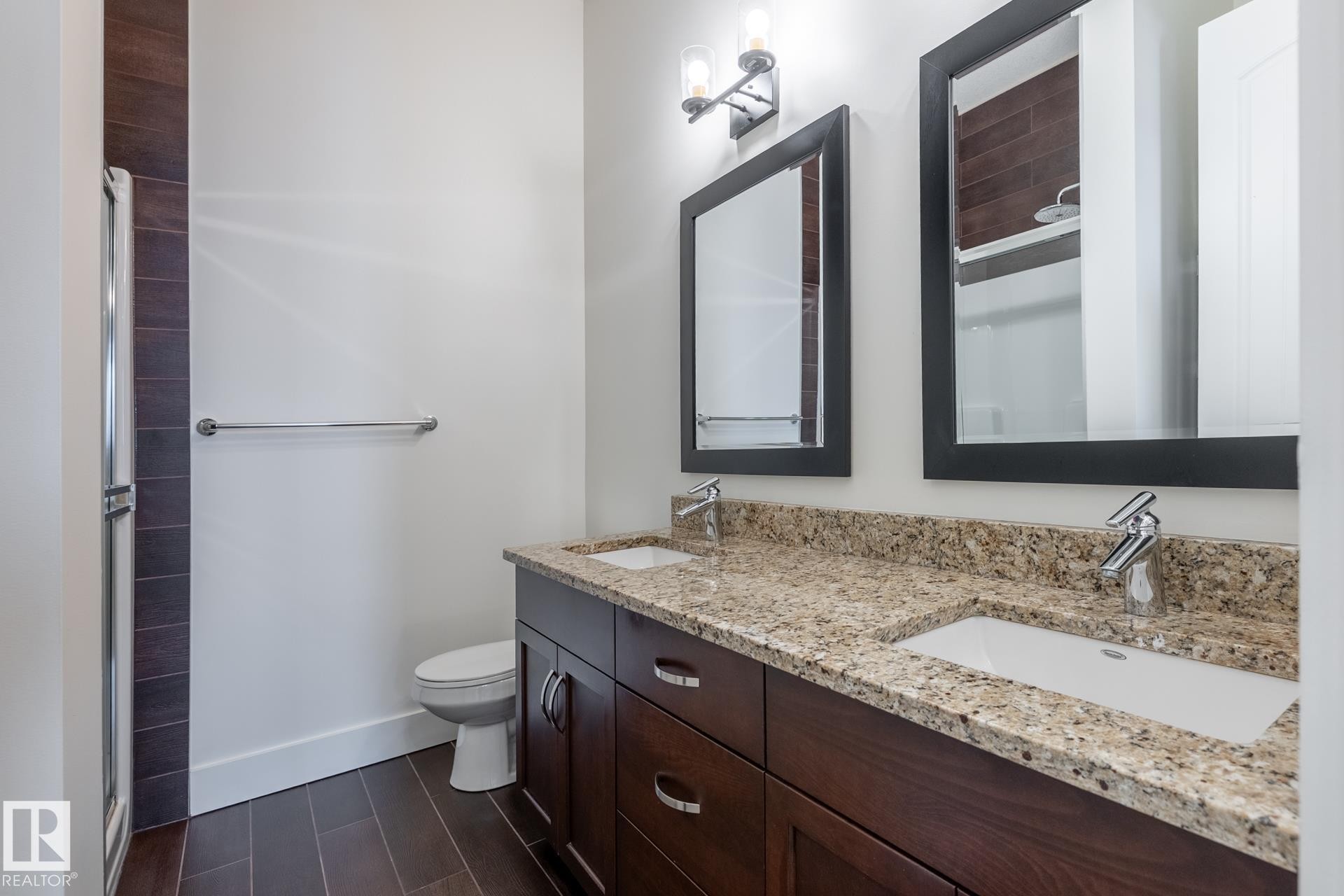 Bathroom featuring a double vanity with granite countertops, undermount sinks, and dark wood cabinetry - 454 6079 Maynard Way, Edmonton, AB - Indoor Photo Showing Bathroom