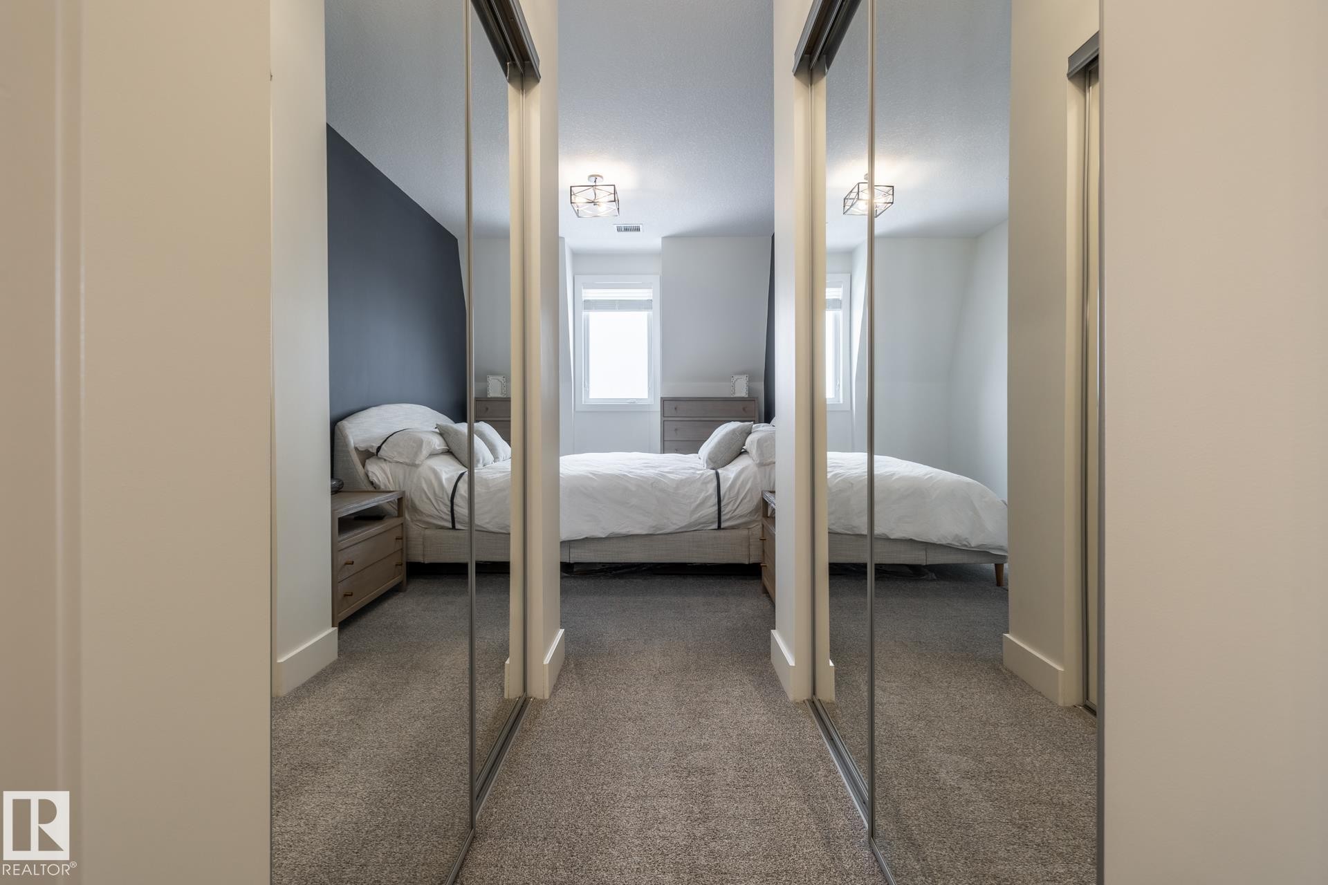 Hallway from ensuite to primary bedroom features mirrored closet doors and carpeted flooring - 454 6079 Maynard Way, Edmonton, AB - Indoor Photo Showing Bedroom