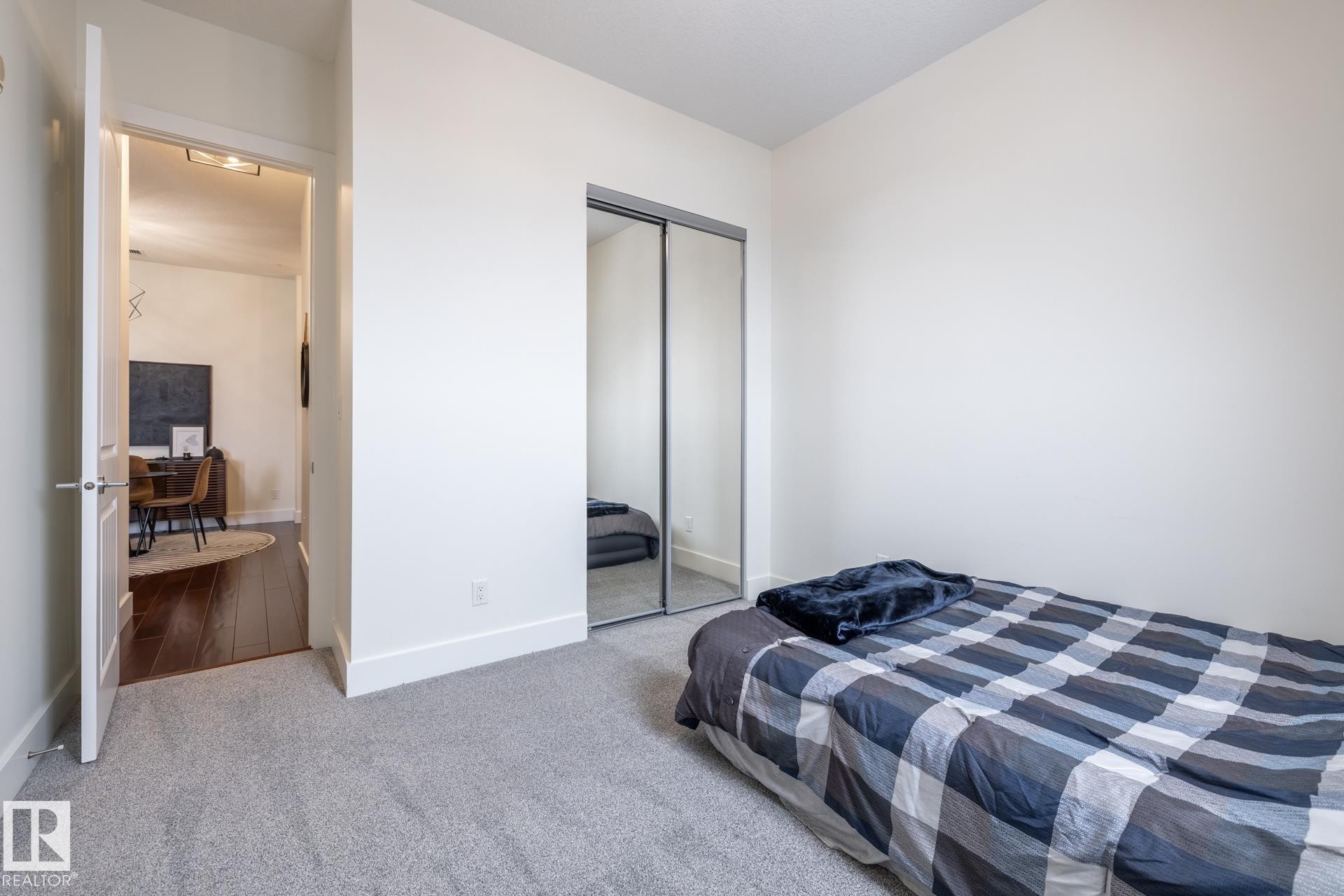 The room features light gray carpeting, white walls, and a mirrored sliding closet door - 454 6079 Maynard Way, Edmonton, AB - Indoor Photo Showing Bedroom