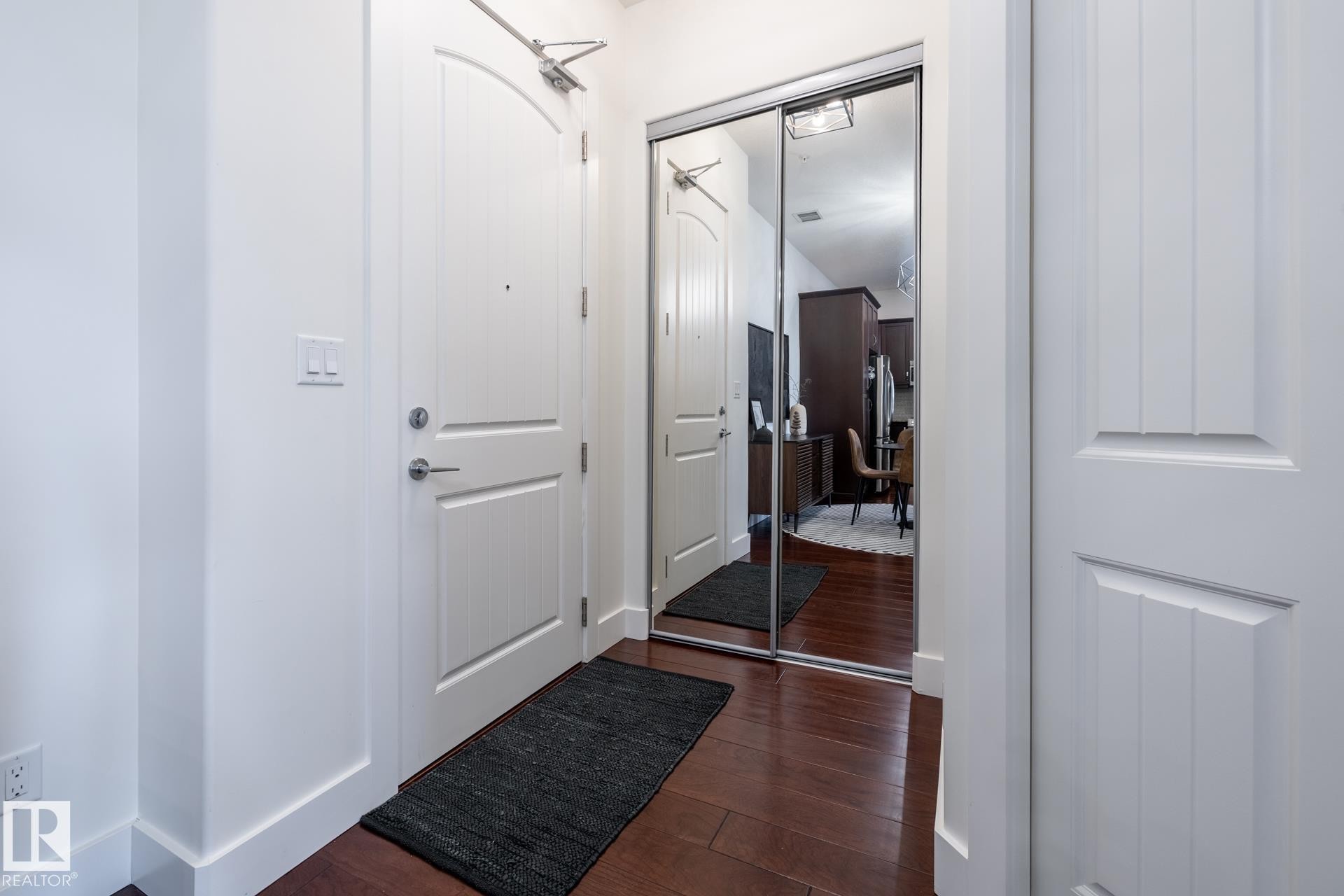 Entryway featuring dark hardwood flooring, a white paneled door, and a mirrored closet with sliding doors - 454 6079 Maynard Way, Edmonton, AB - Indoor Photo Showing Other Room