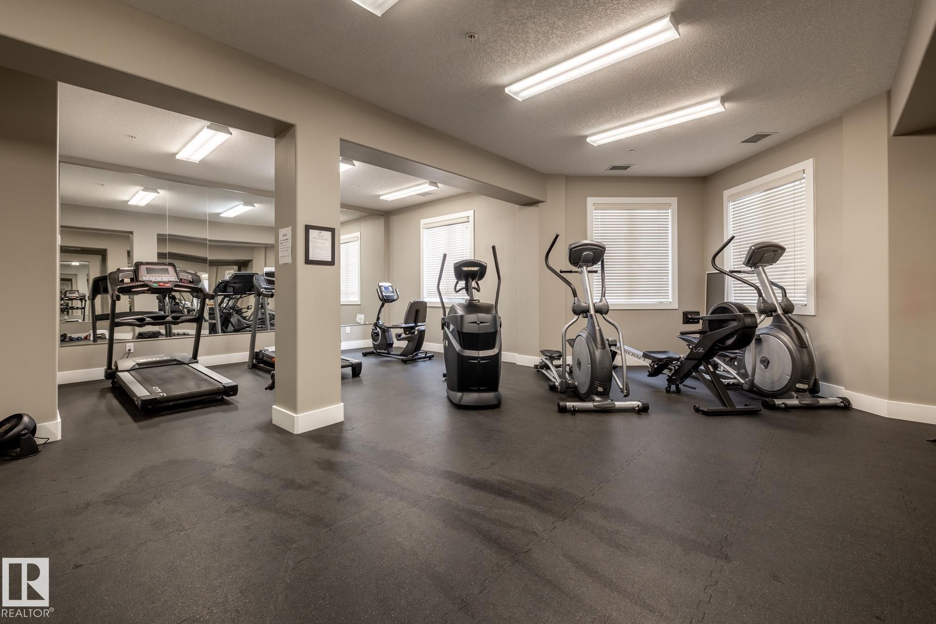 The property features a well-equipped fitness area with various exercise machines, including treadmills and ellipticals - 454 6079 Maynard Way, Edmonton, AB - Indoor Photo Showing Gym Room