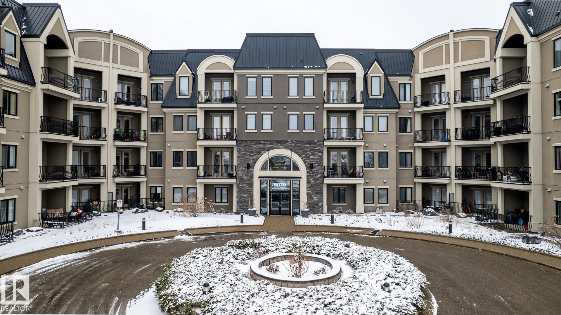 The property features a multi-story facade with balconies, a central arched entrance, and a stone accent wall - 454 6079 Maynard Way, Edmonton, AB - Outdoor With Facade