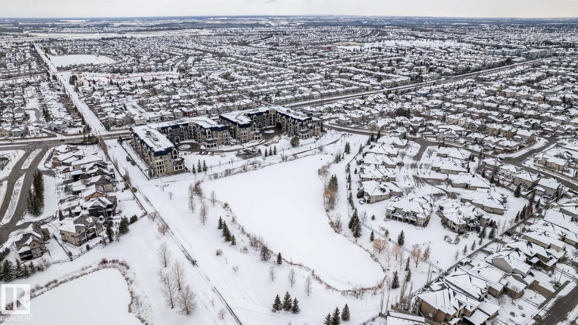 Aerial view of the community, showcasing residential properties and a central pond, all covered in snow - 454 6079 Maynard Way, Edmonton, AB - Outdoor With View