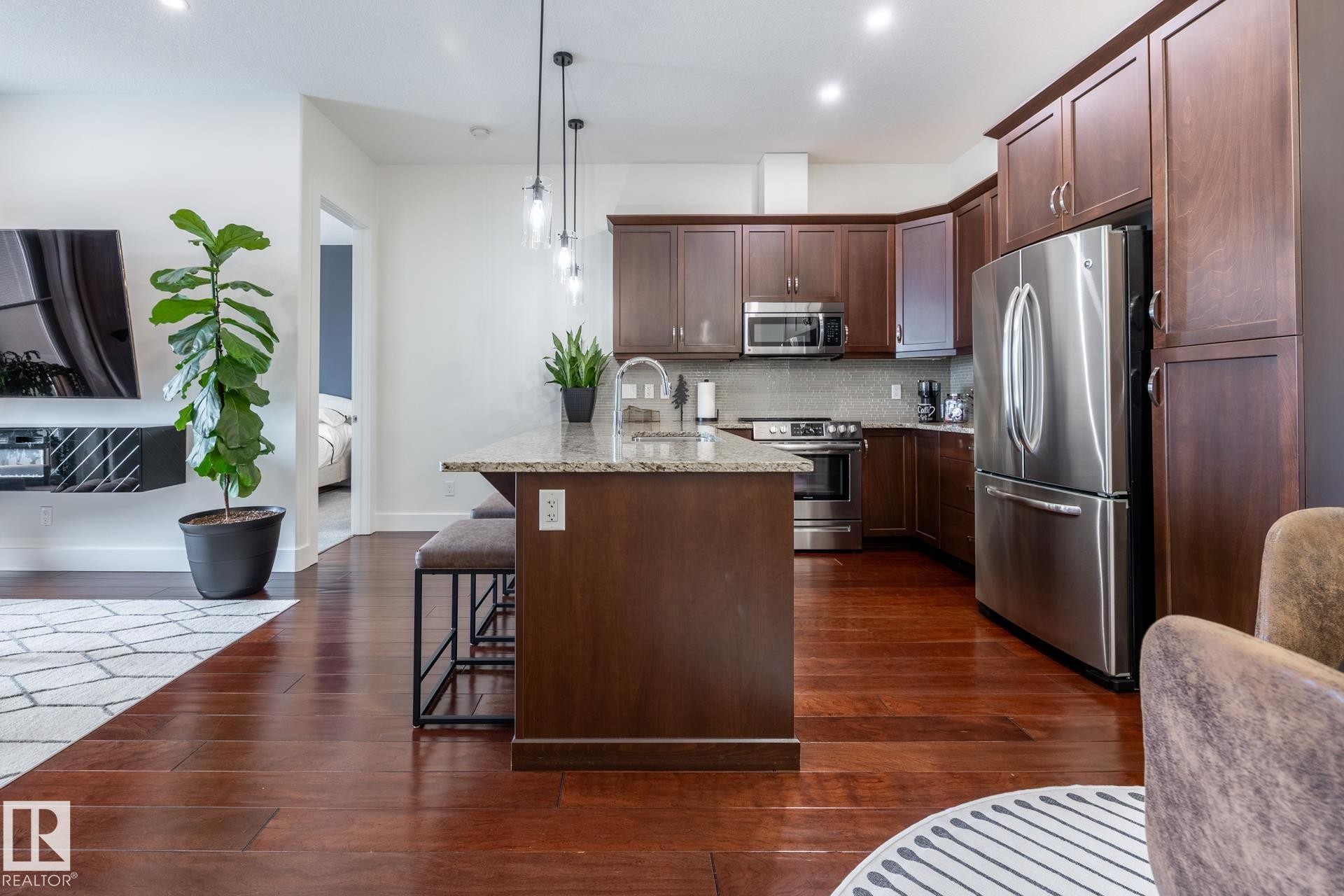 Kitchen featuring rich wood cabinetry, stainless steel appliances, a granite countertop island, and pendant lighting - 454 6079 Maynard Way, Edmonton, AB - Indoor Photo Showing Kitchen