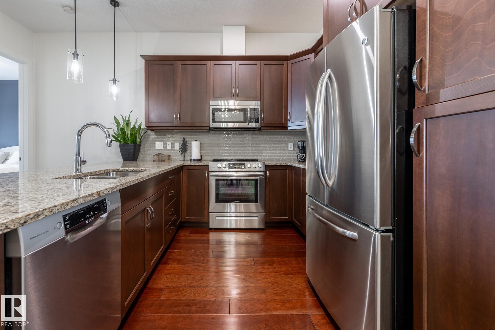 The kitchen features hardwood floors, granite countertops, stainless steel appliances, and dark wood cabinetry - 454 6079 Maynard Way, Edmonton, AB - Indoor Photo Showing Kitchen With Double Sink With Upgraded Kitchen