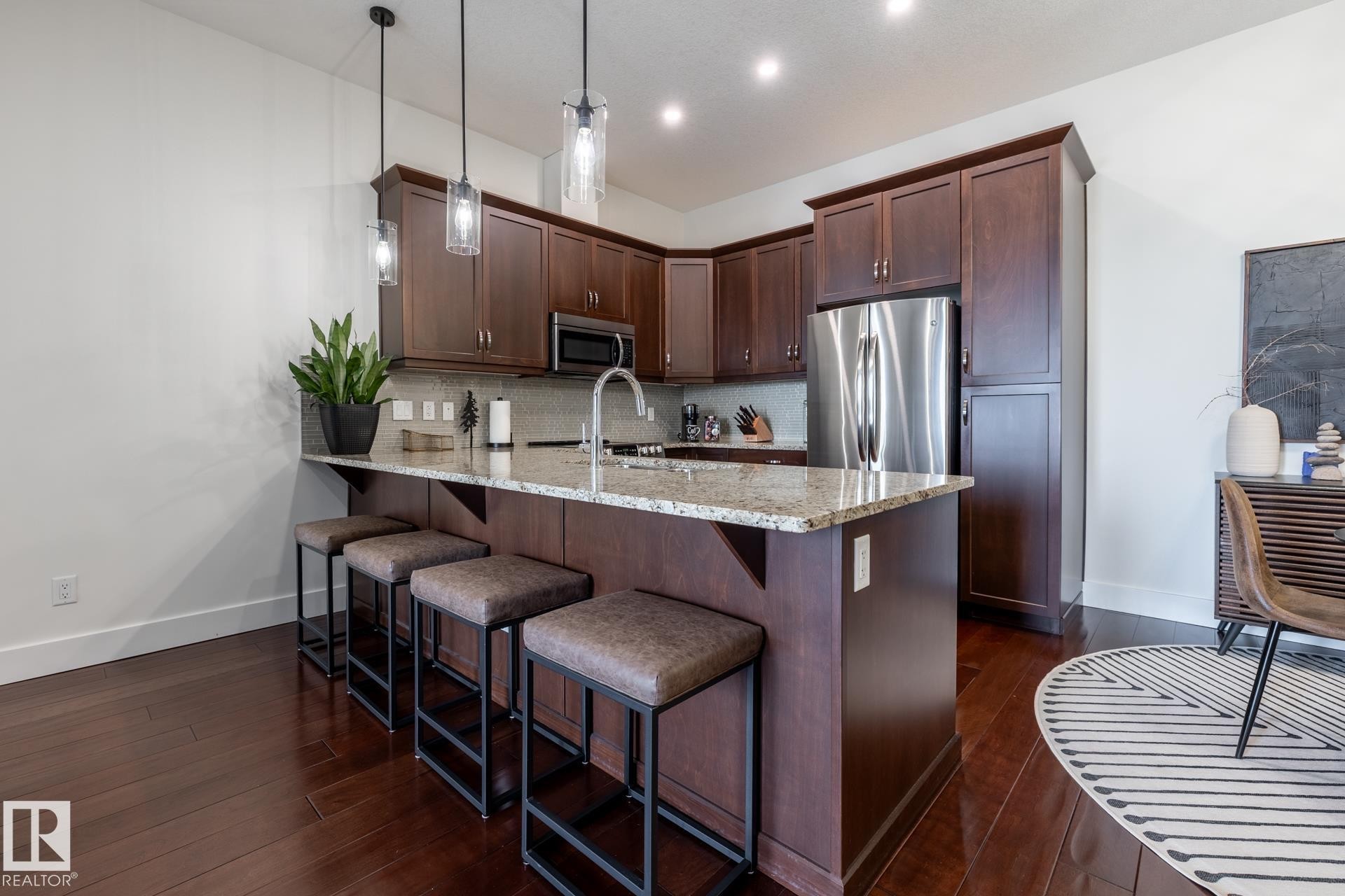 The kitchen features dark wood cabinetry, stainless steel appliances, and a light-colored granite countertop - 454 6079 Maynard Way, Edmonton, AB - Indoor Photo Showing Kitchen With Upgraded Kitchen