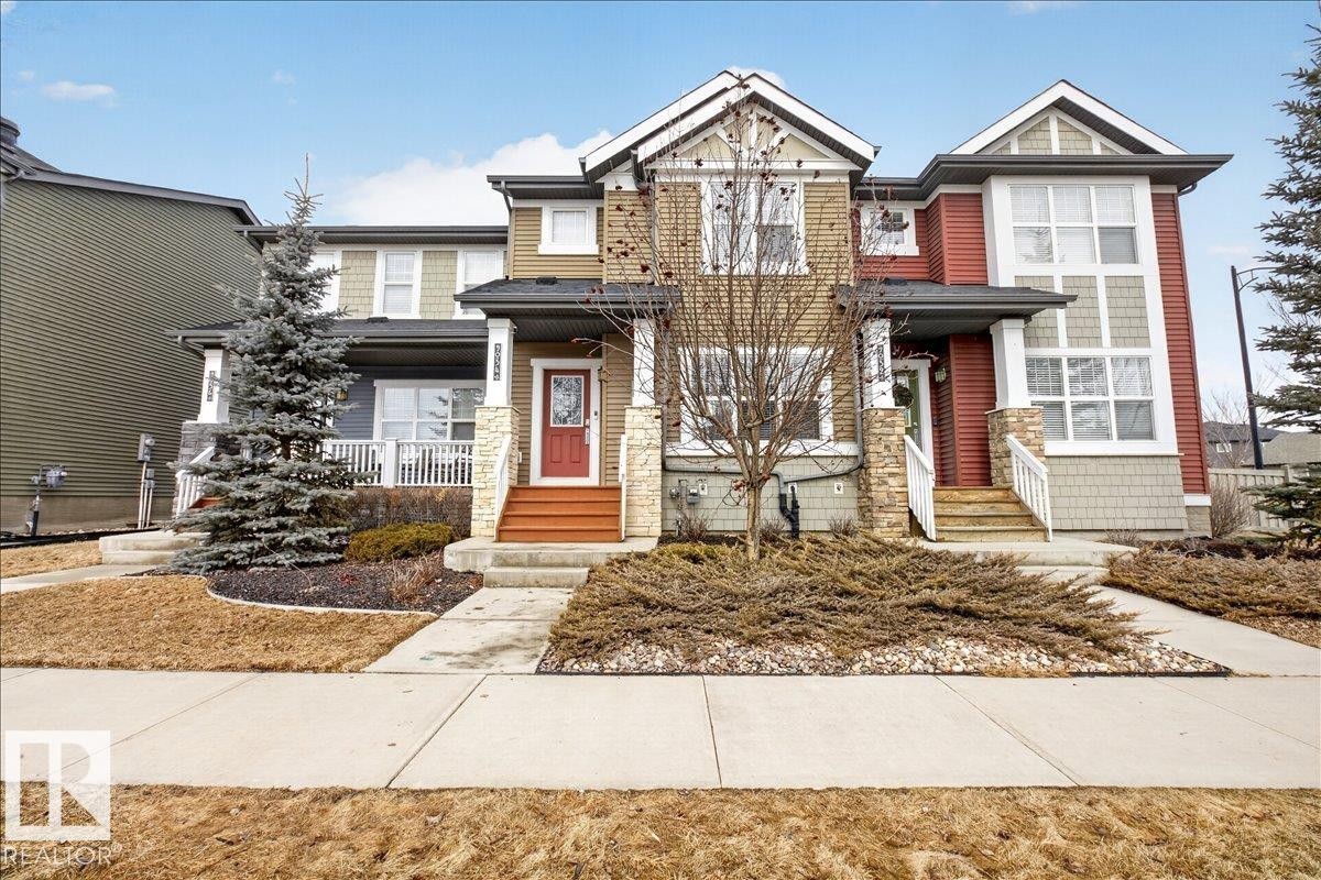 The property features a stone facade and a red front door, complemented by a front porch with white railings - 9034 Rosenthal Link, Edmonton, AB - Outdoor With Facade