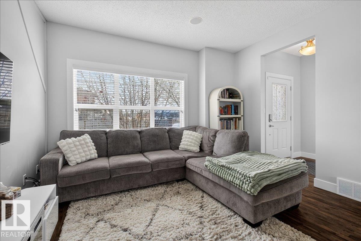 Living room with bright white walls, dark wood flooring, and a large window with white blinds - 9034 Rosenthal Link, Edmonton, AB - Indoor Photo Showing Living Room