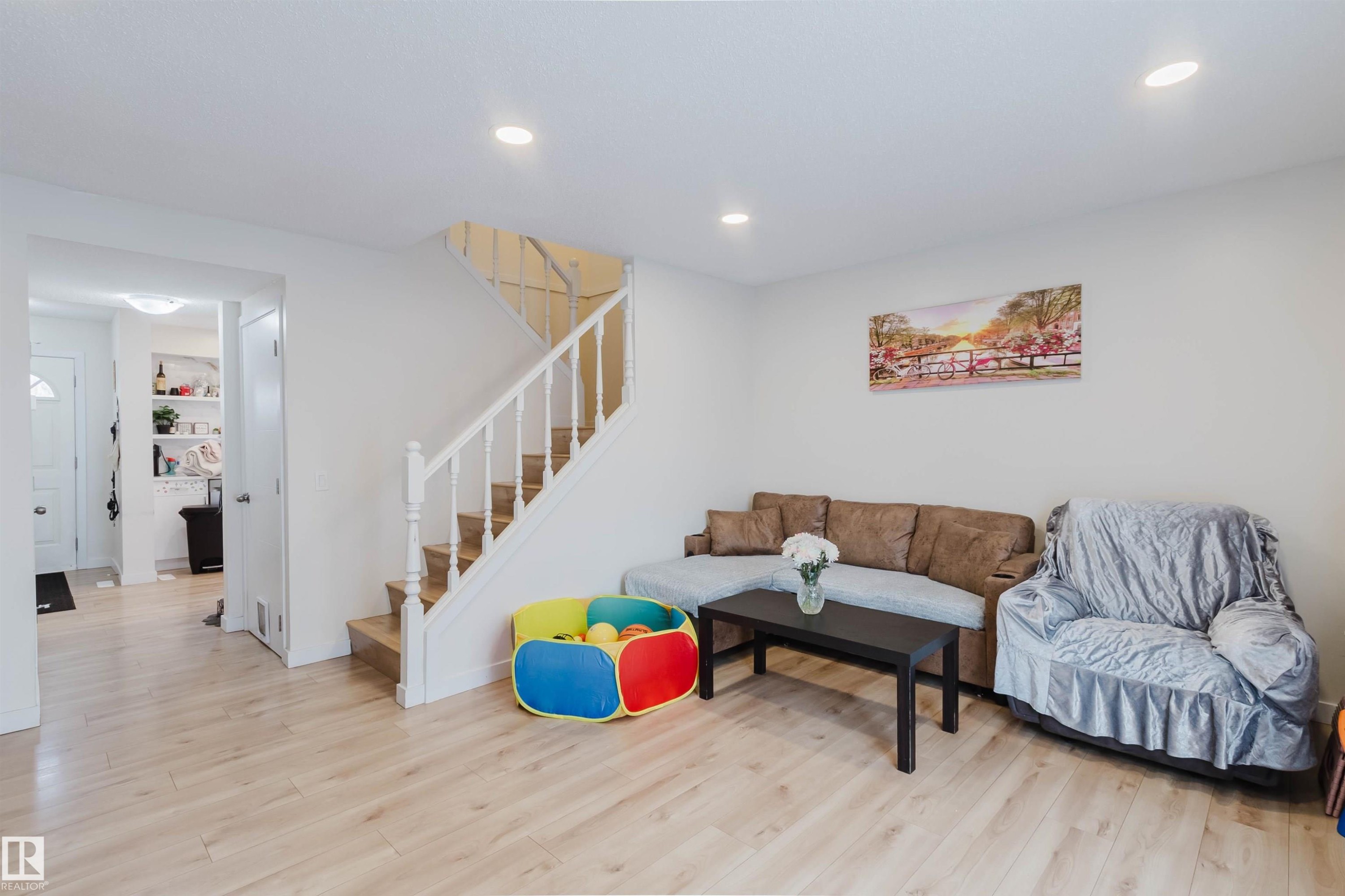 This bright living area features light-toned flooring, a staircase with white railings, and recessed ceiling lights - 18088 93 Avenue Nw, Edmonton, AB - Indoor Photo Showing Living Room