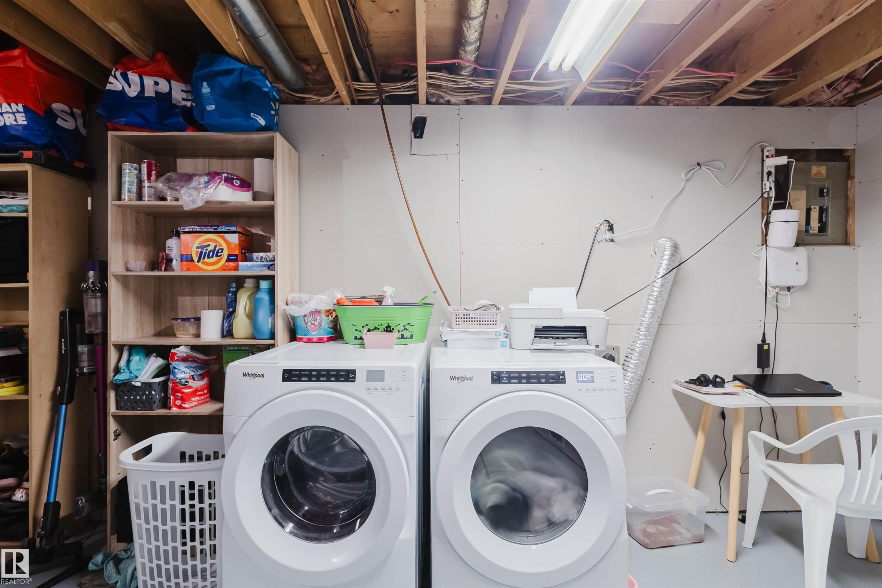 Laundry area featuring two front-loading machines, built-in shelving, and a utility table - 18088 93 Avenue Nw, Edmonton, AB - Indoor Photo Showing Laundry Room