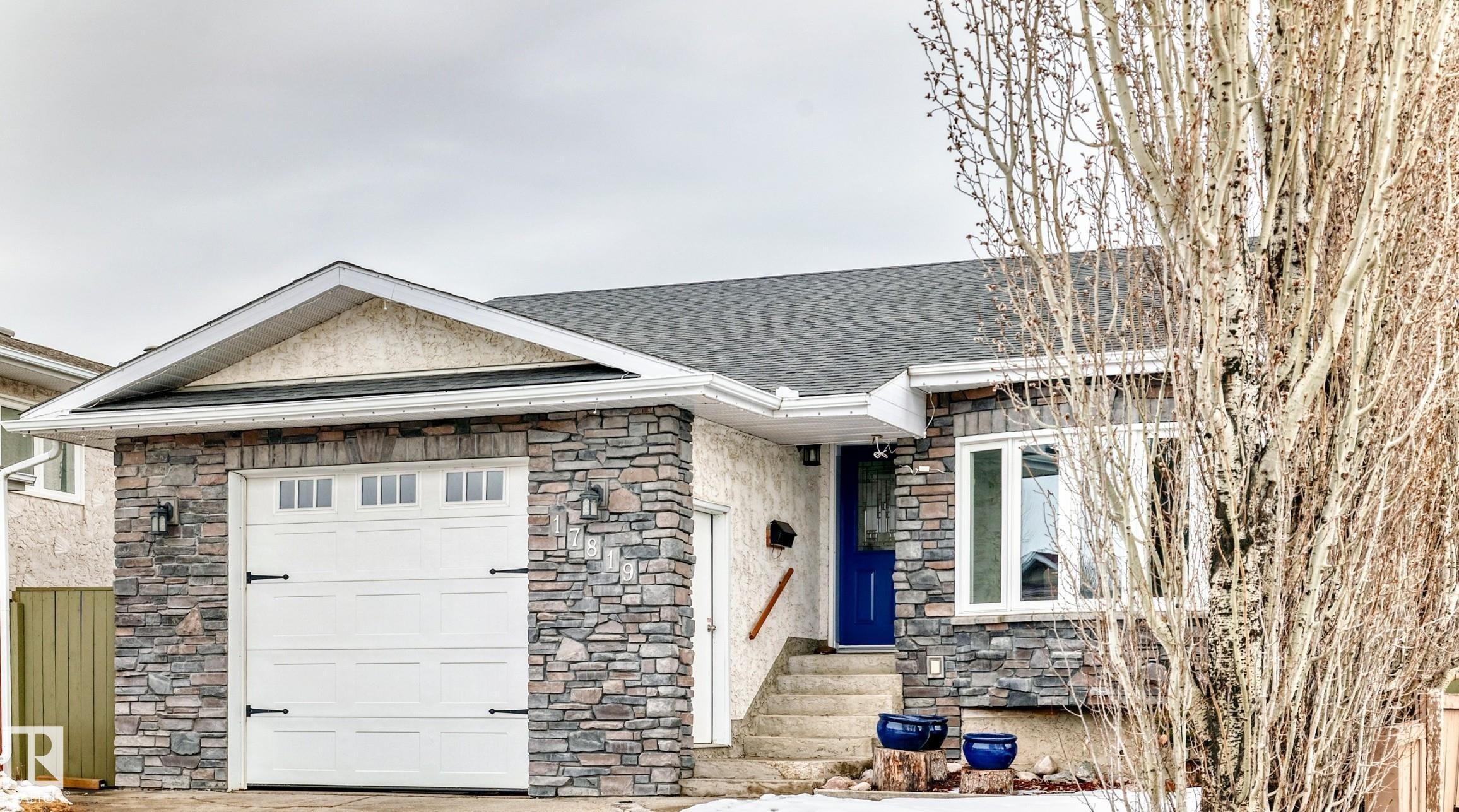 The property features a stone facade, a white garage door with decorative hardware, and a vibrant blue entry door - 17819 91A Street, Edmonton, AB - Outdoor
