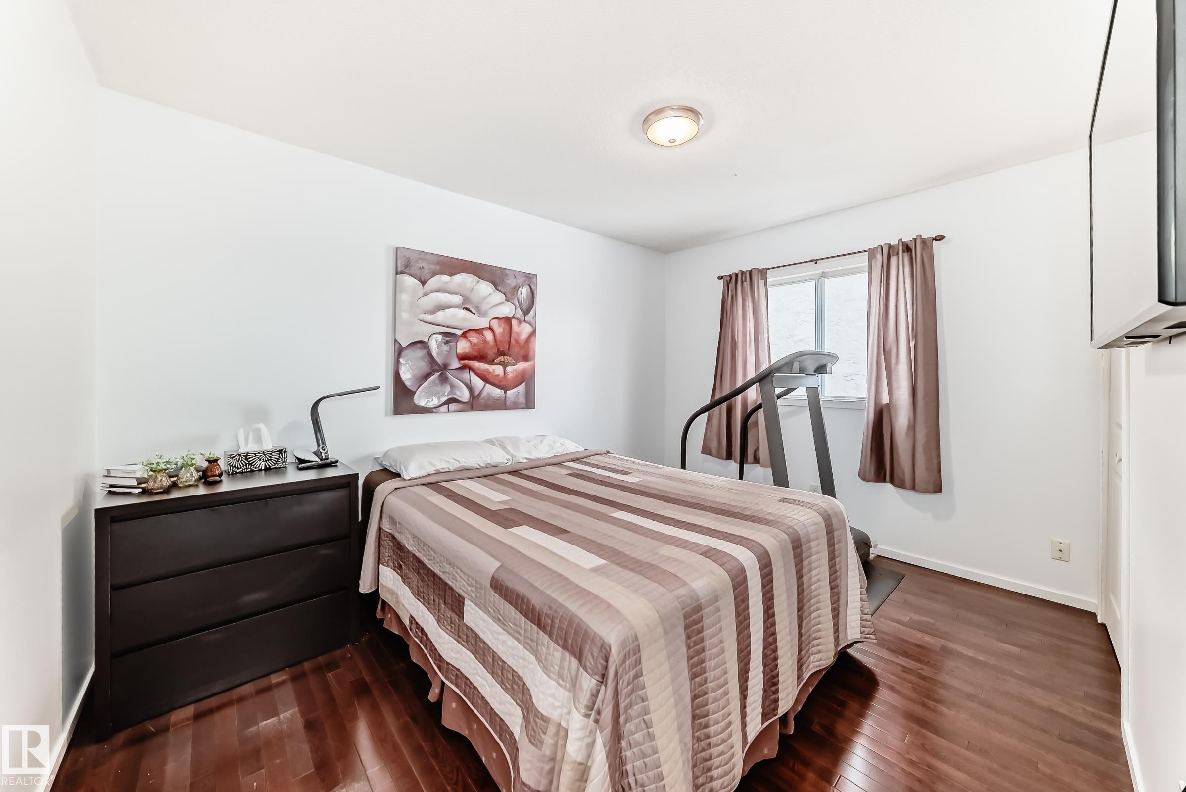 This room features hardwood floors, a ceiling light fixture, a window with curtains, and a wall-mounted display - 17819 91A Street, Edmonton, AB - Indoor Photo Showing Bedroom