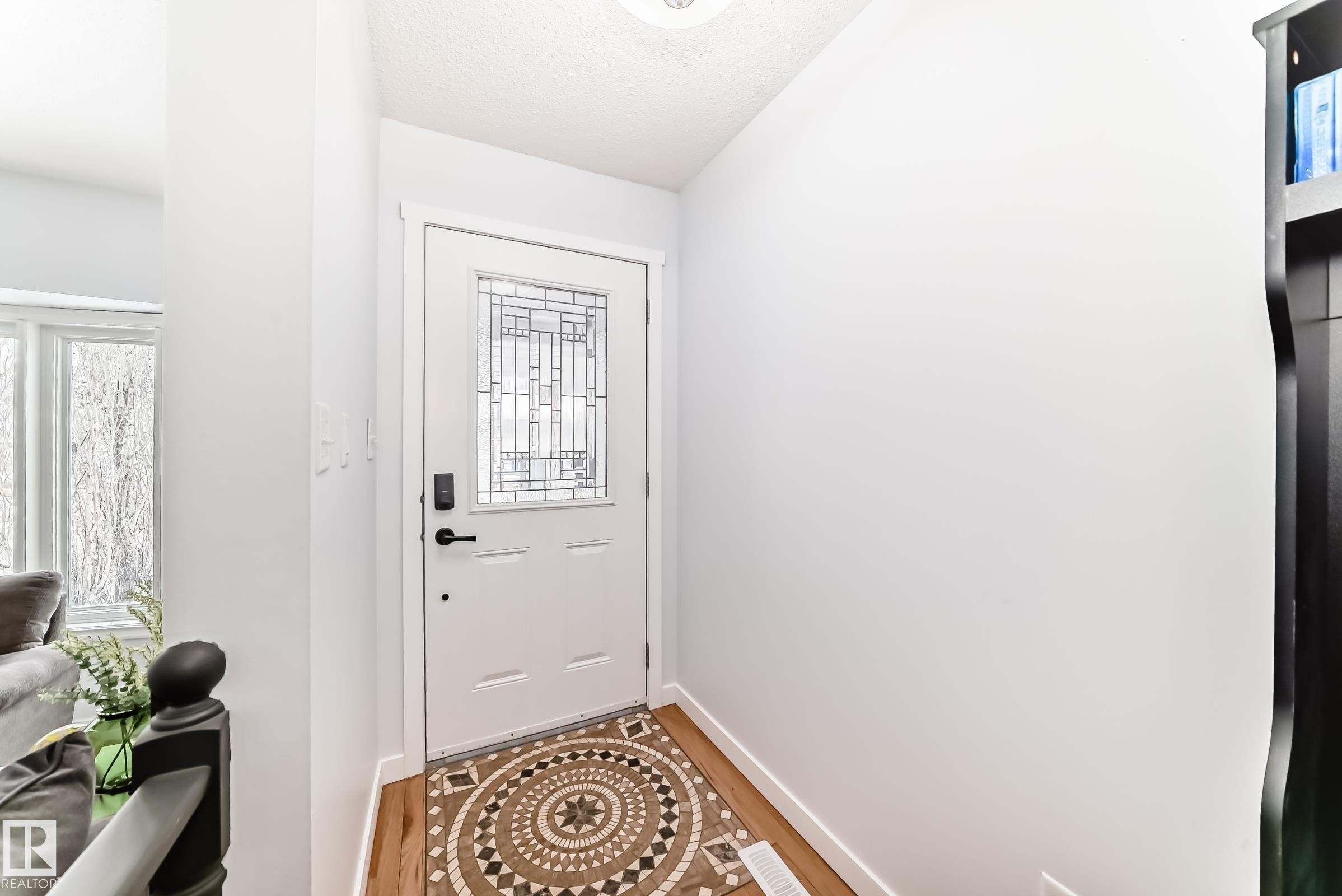 The entryway features a white door with decorative leaded glass and a patterned mat, set against light-colored walls and hardwood flooring - 17819 91A Street, Edmonton, AB - Indoor Photo Showing Other Room