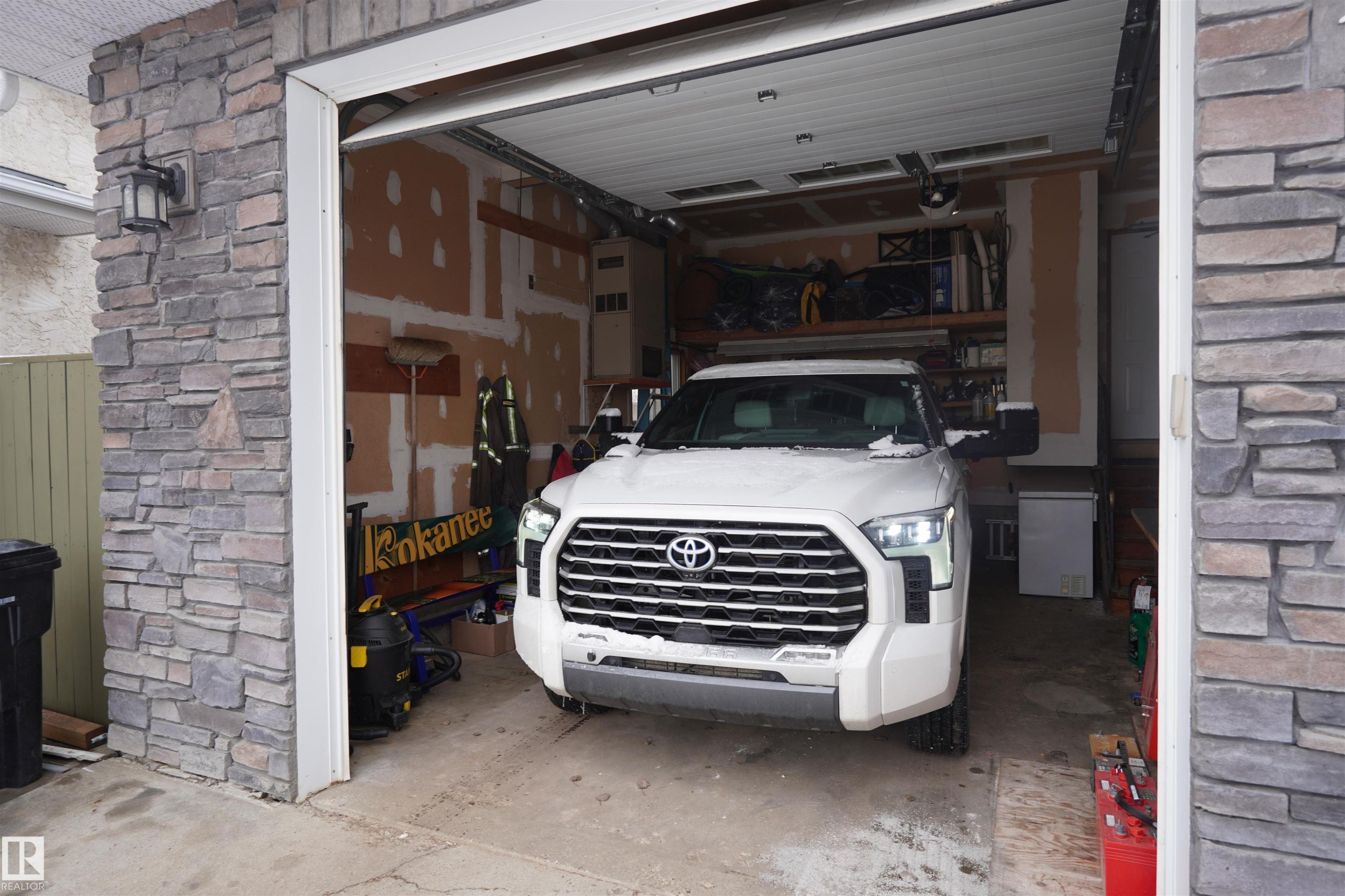 The property features an attached garage with a stone facade, an overhead garage door, and interior shelving for storage - 17819 91A Street, Edmonton, AB -