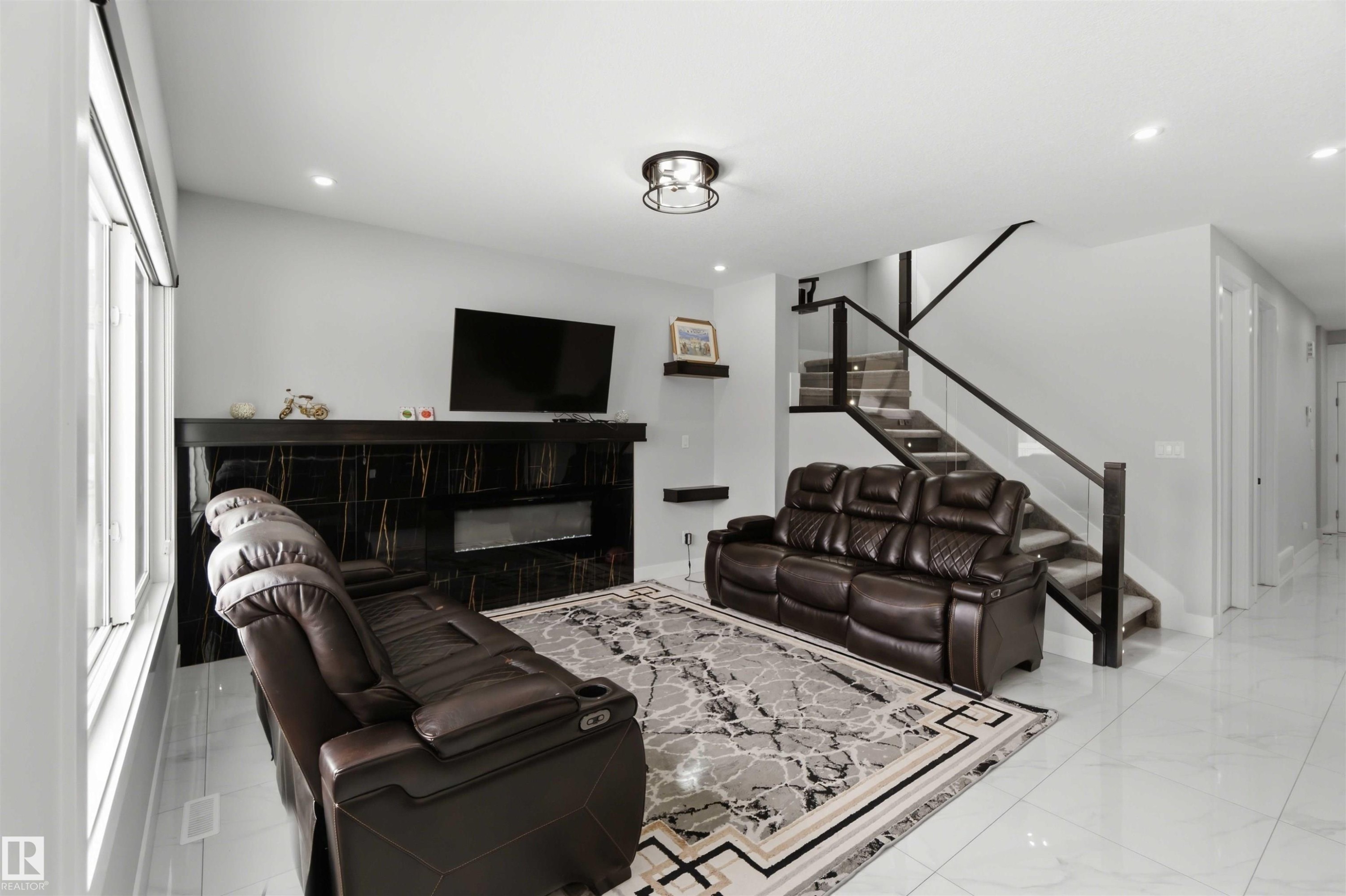 The living area features a modern fireplace with a black marble-style surround, large windows, and sleek tile flooring - 1520 151 Avenue, Edmonton, AB - Indoor