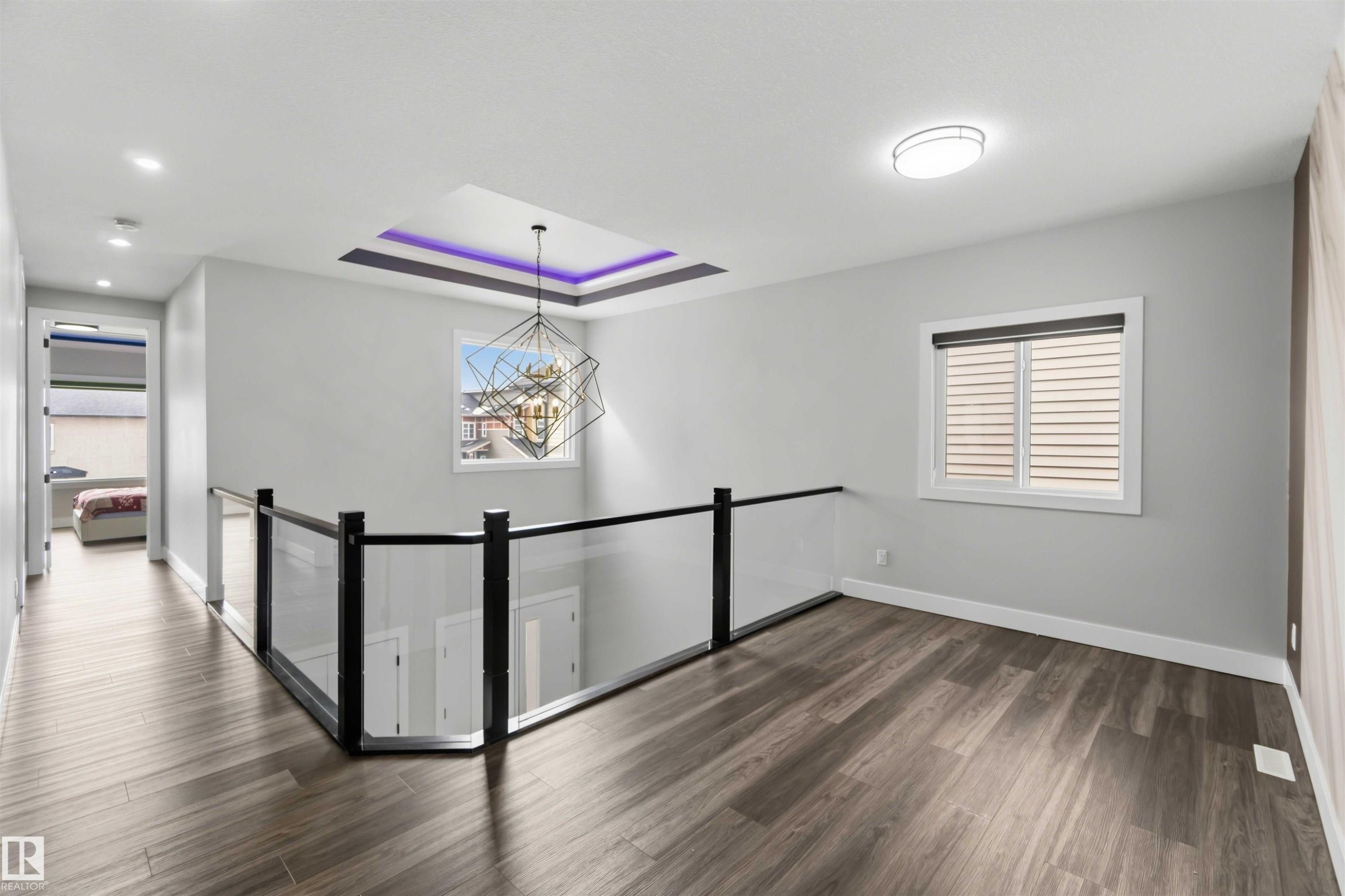 This upstairs landing features wood-look flooring, a modern geometric chandelier with purple accent lighting, and a glass and black railing - 1520 151 Avenue, Edmonton, AB - Indoor Photo Showing Other Room