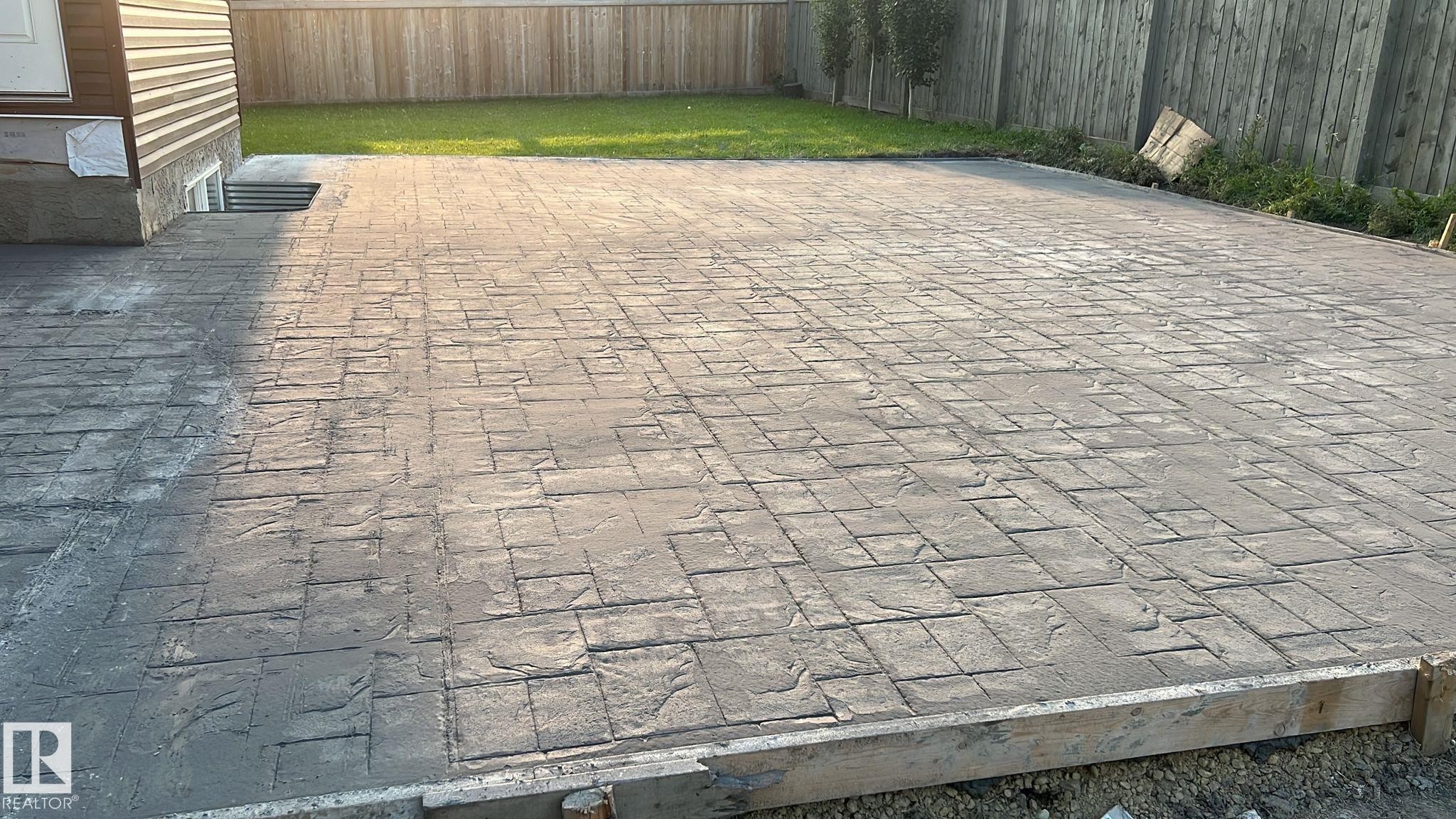 The property features an expansive stamped concrete patio with a textured pattern - 1520 151 Avenue, Edmonton, AB - Outdoor