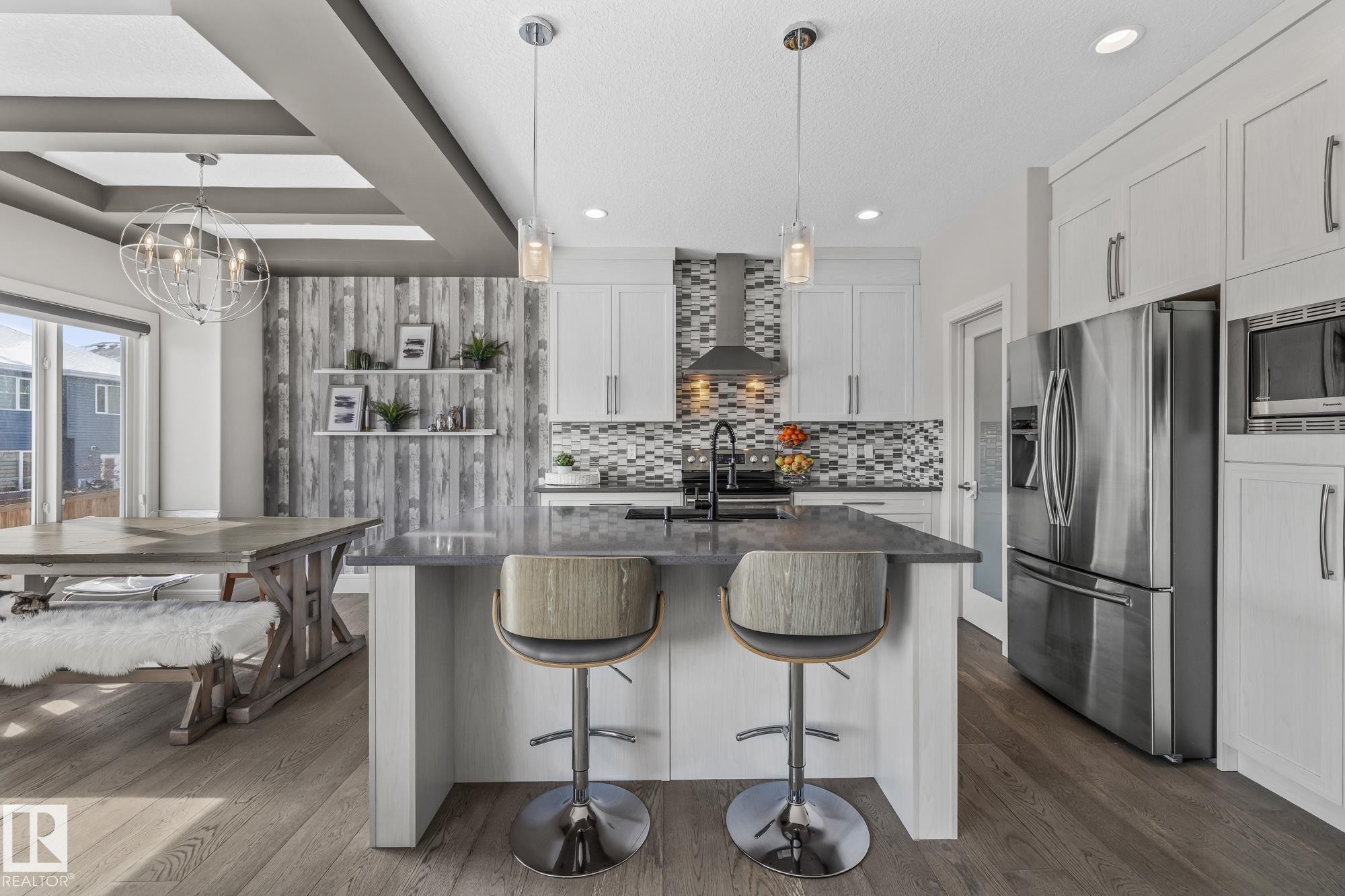 The kitchen features white cabinetry, stainless steel appliances, a mosaic tile backsplash, and a central island with bar seating - 3864 Robins Crescent, Edmonton, AB - Indoor Photo Showing Kitchen With Upgraded Kitchen