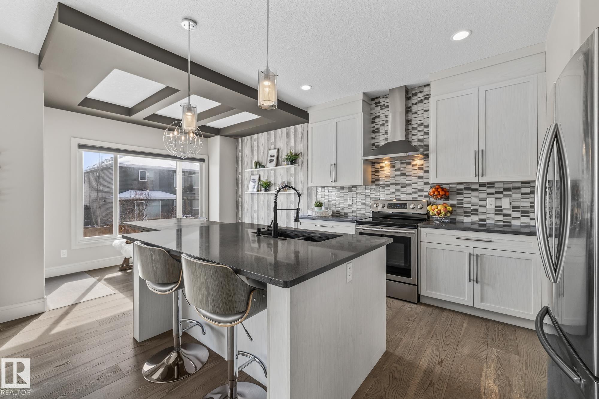 The kitchen features a spacious island with a dark countertop, white cabinetry, a stylish tiled backsplash, and stainless steel appliances - 3864 Robins Crescent, Edmonton, AB - Indoor Photo Showing Kitchen With Upgraded Kitchen