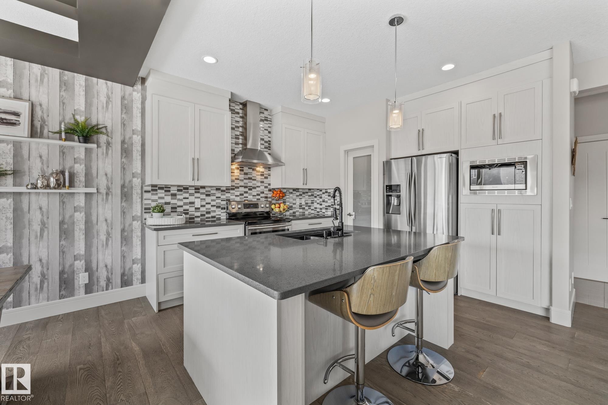 The kitchen features white cabinetry, stainless steel appliances, a mosaic tile backsplash, and a central island with a dark countertop and pendant lighting - 3864 Robins Crescent, Edmonton, AB - Indoor Photo Showing Kitchen With Double Sink With Upgraded Kitchen