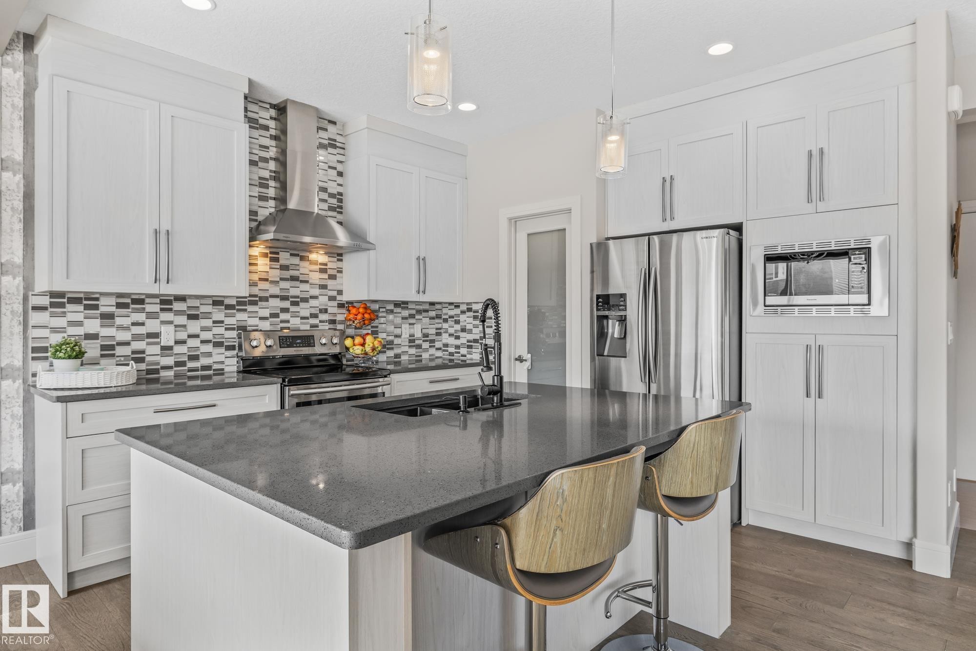 The kitchen features an island with a dark countertop and seating, white cabinetry, and stainless steel appliances - 3864 Robins Crescent, Edmonton, AB - Indoor Photo Showing Kitchen With Upgraded Kitchen