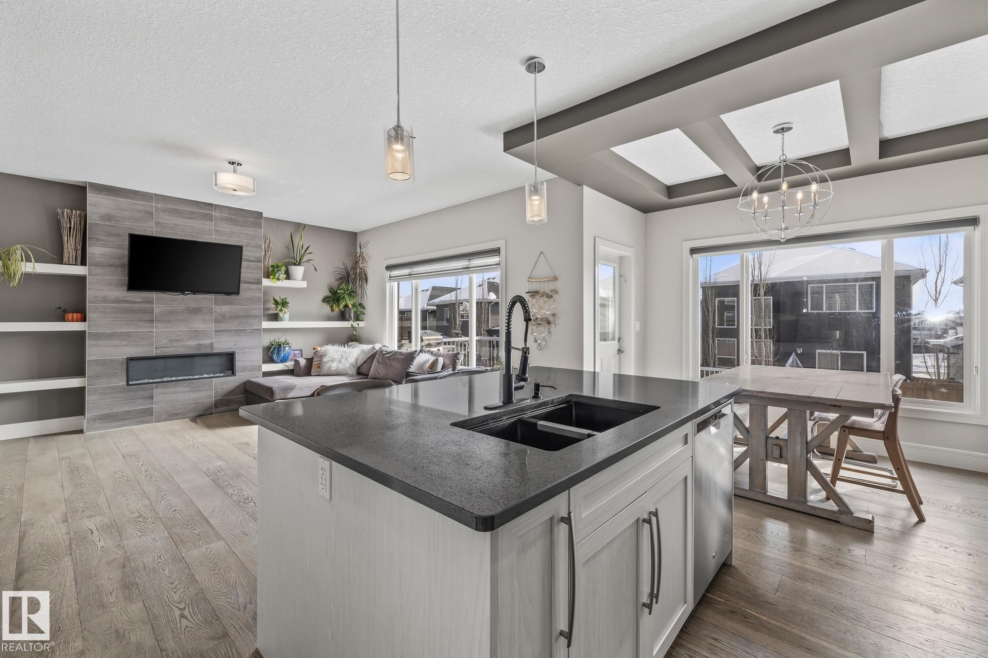 Open concept living area featuring hardwood floors, a kitchen island with a dark countertop and double sink, and large windows - 3864 Robins Crescent, Edmonton, AB - Indoor Photo Showing Kitchen With Fireplace With Double Sink
