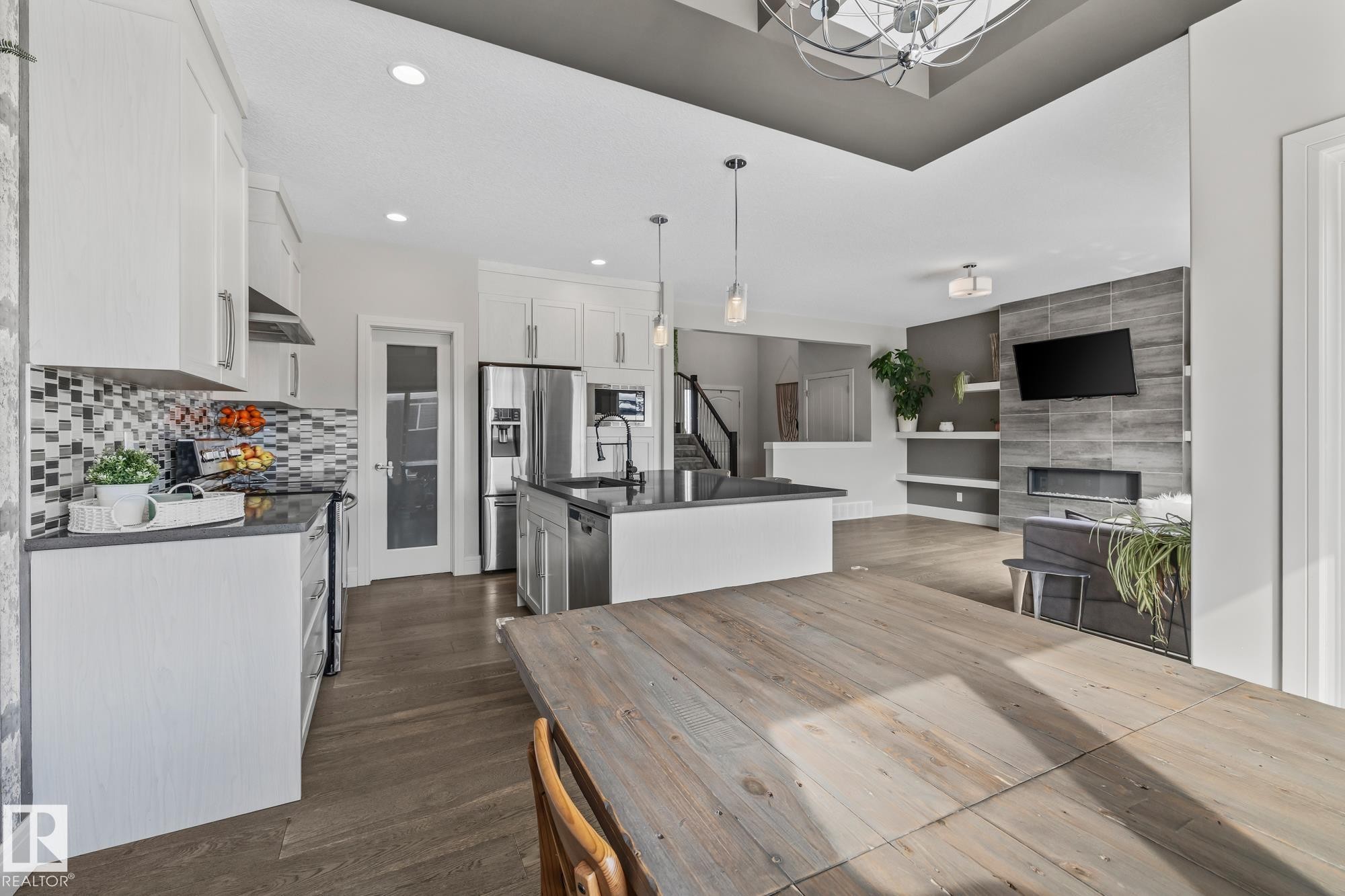 The property features a kitchen with white cabinetry, a tiled backsplash, and stainless steel appliances, including a refrigerator and a range hood - 3864 Robins Crescent, Edmonton, AB - Indoor With Fireplace