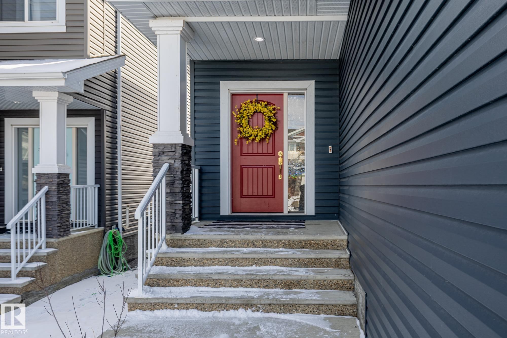 The property features a bold red entry door with a sidelight, set under a covered porch with white columns and stone accents - 3864 Robins Crescent, Edmonton, AB - Outdoor