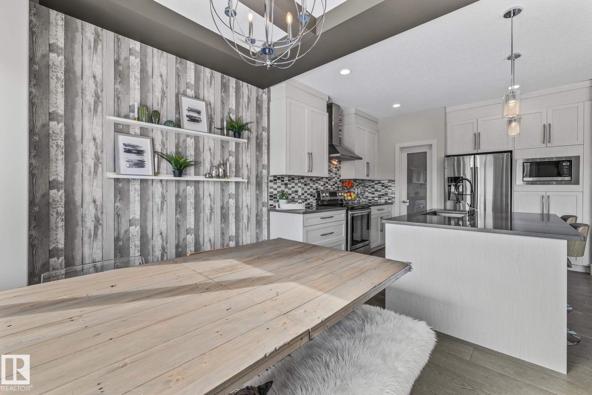 This inviting dining area features a large light wood table, a decorative accent wall with shelving, and a contemporary chandelier - 3864 Robins Crescent, Edmonton, AB - Indoor Photo Showing Kitchen With Upgraded Kitchen