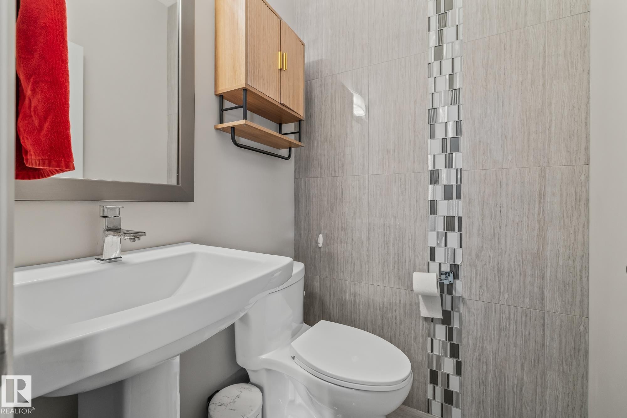 Powder room featuring a sleek white sink with a modern faucet, a wooden wall-mounted cabinet with open shelving, and stylish gray wall tiles with a decorative mosaic accent - 3864 Robins Crescent, Edmonton, AB - Indoor Photo Showing Bathroom