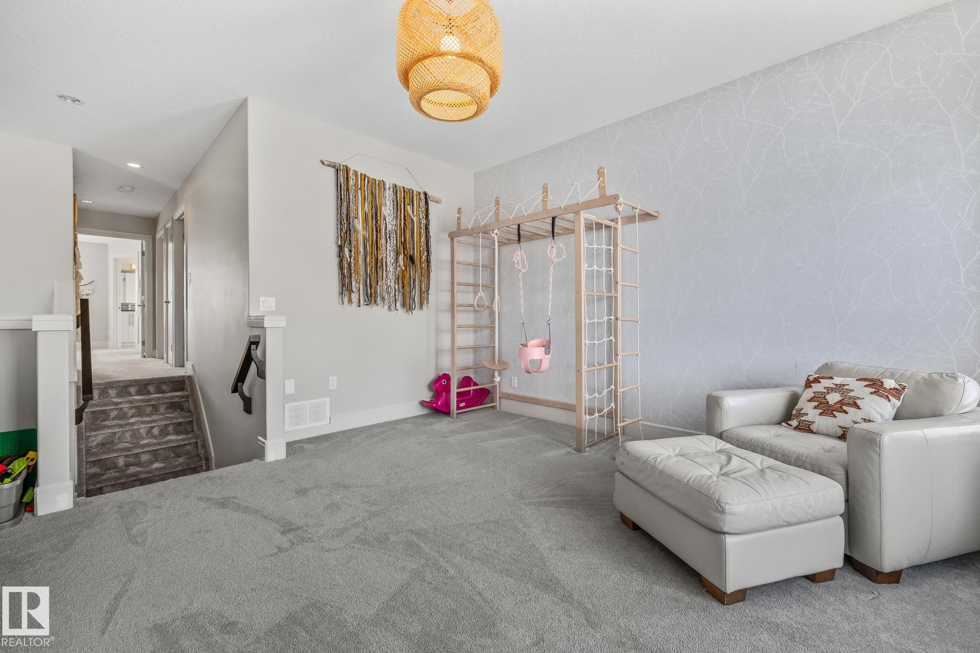 This spacious room features gray carpeting, light gray walls with a decorative accent wall, and a staircase with gray carpeted steps - 3864 Robins Crescent, Edmonton, AB - Indoor Photo Showing Other Room
