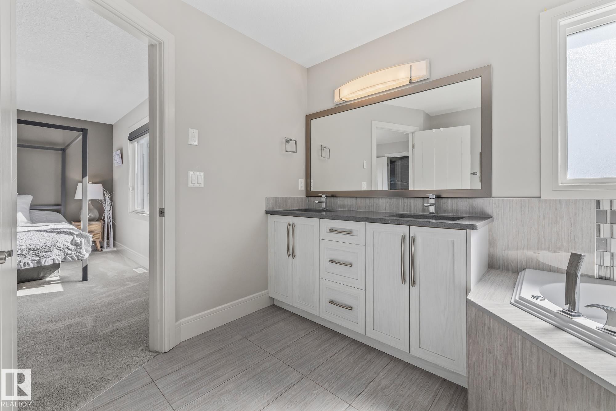Bathroom featuring a double vanity with white cabinetry, a large mirror, and a bathtub with tile surround - 3864 Robins Crescent, Edmonton, AB - Indoor Photo Showing Bathroom