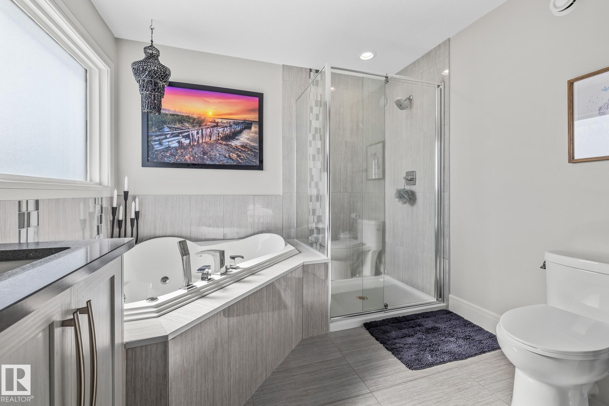Bright bathroom featuring a large window, a jetted corner bathtub, a walk-in shower with a glass door, a vanity with a dark countertop, and tiled floors - 3864 Robins Crescent, Edmonton, AB - Indoor Photo Showing Bathroom